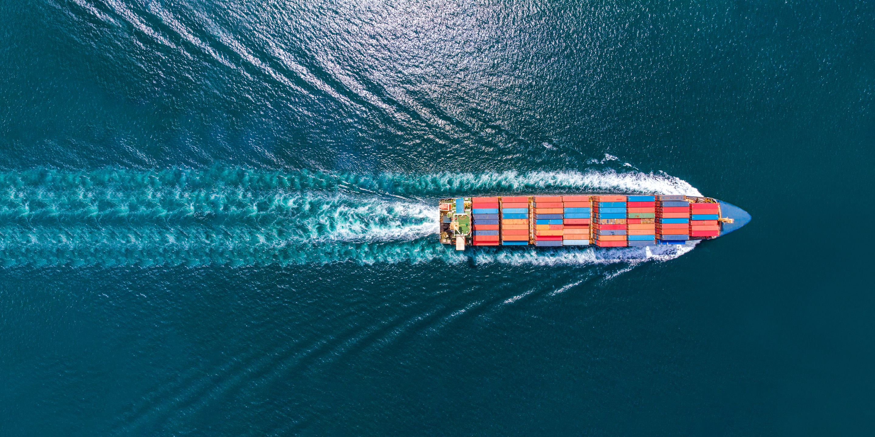 Aerial top view of cargo ship with contrail in the ocean sea ship carrying container and running for export cargo from container international yard port to custom ocean concept freight shipping by ship service .