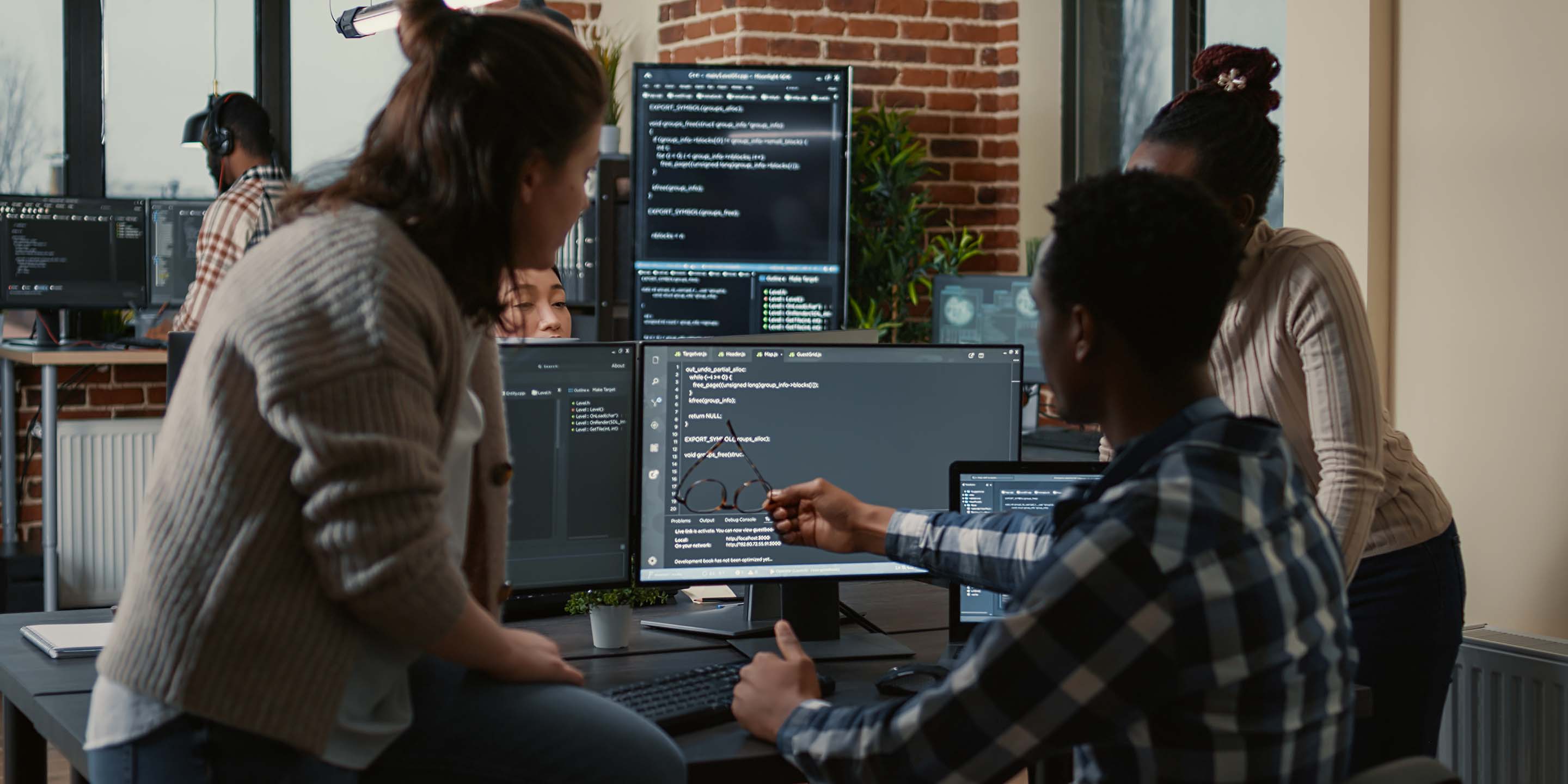 Programer sitting on desk discussing with mixed team of software developers about artificial intelligence innovation. Programmers doing teamwork looking at running machine learning algorithms.