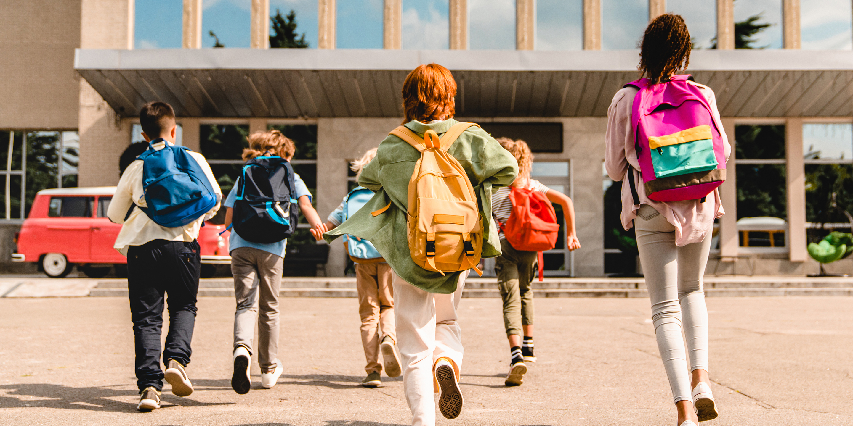Little kids schoolchildren pupils students running hurrying to the school building for classes lessons from to the school bus. Welcome back to school. The new academic semester year start