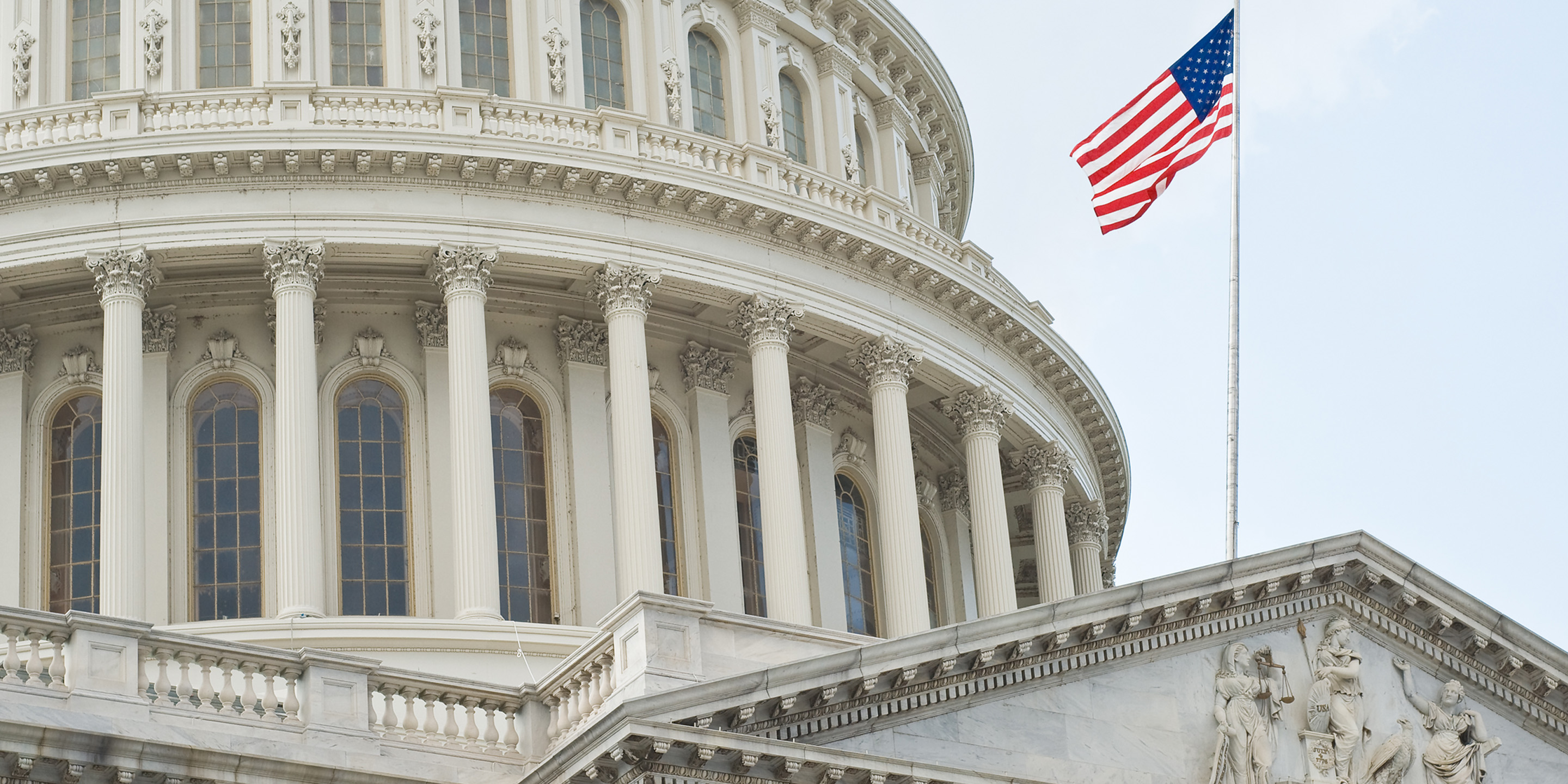 American flag waves beside dome of historic Capitol building.