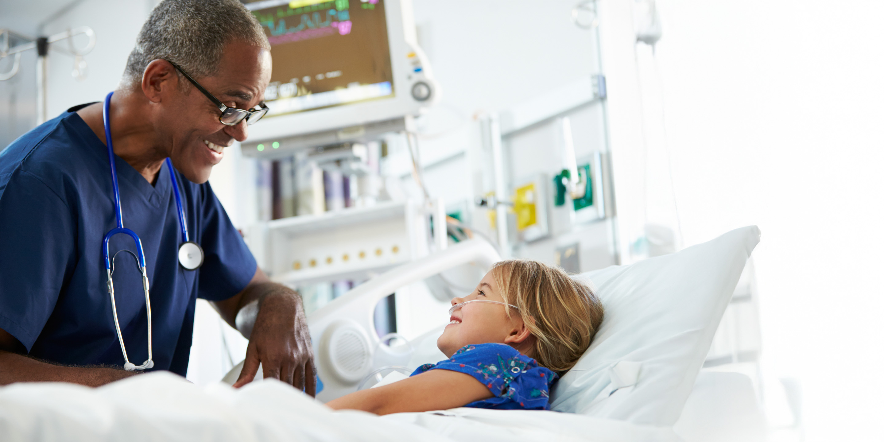 Doctor speaks to patient resting in hospital bed, equipment nearby.