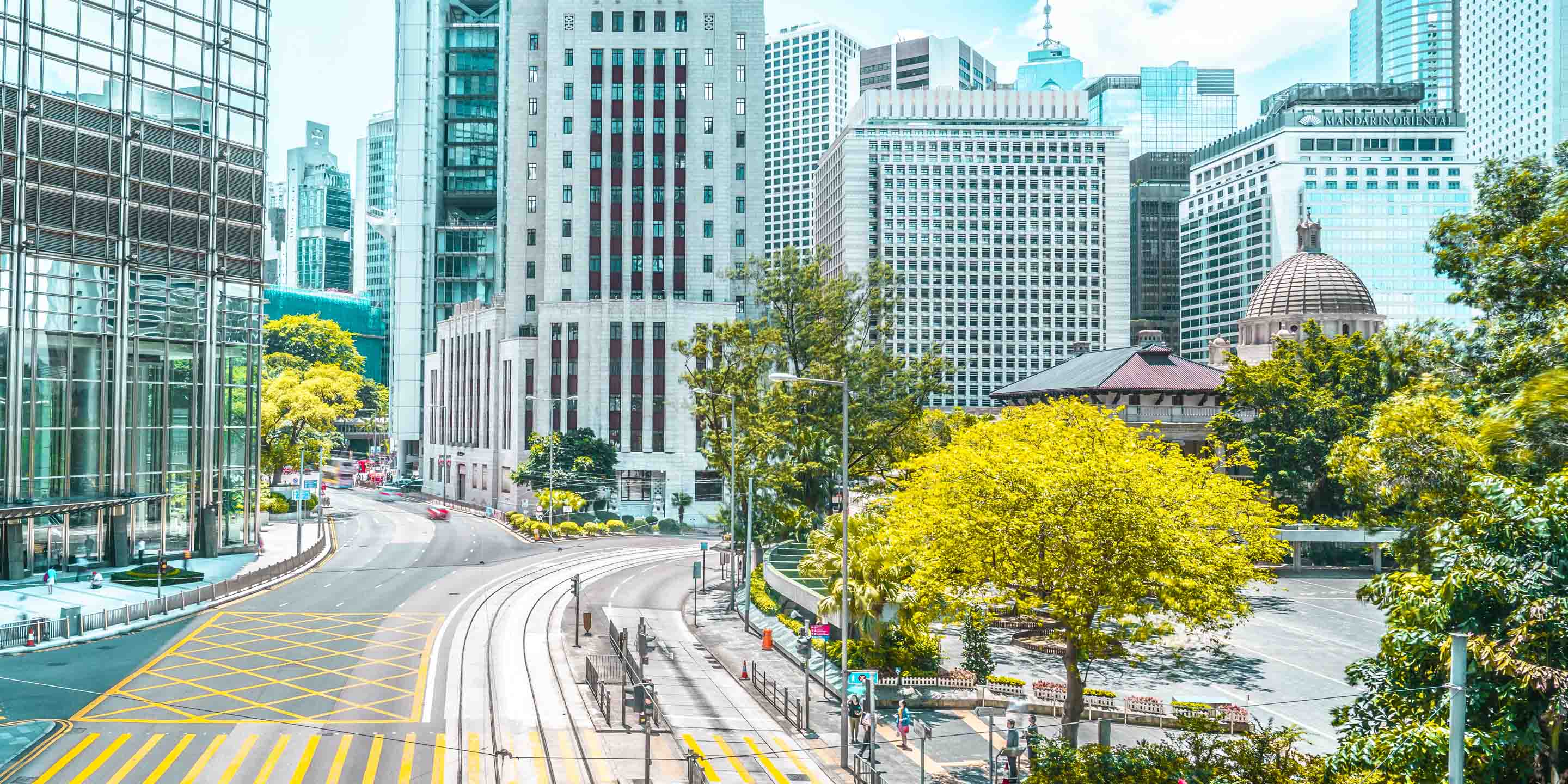 Discover a vibrant urban scene featuring towering modern buildings, a gracefully curved road, and lush greenery lining the sidewalks. This cityscape captures the dynamic blend of architecture and nature in contemporary city planning.