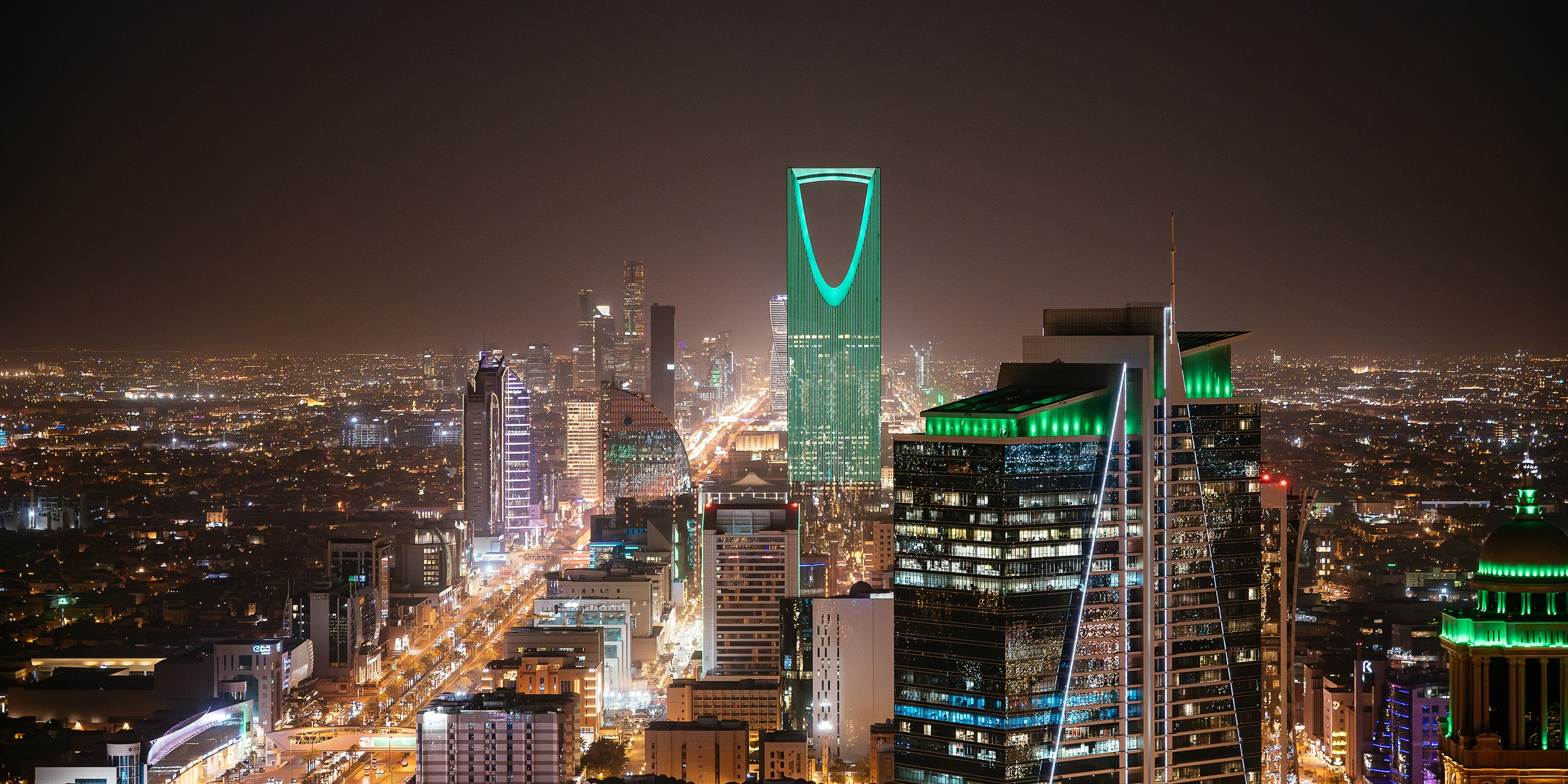 Illuminated Riyadh skyline at night featuring the iconic Kingdom Centre tower.