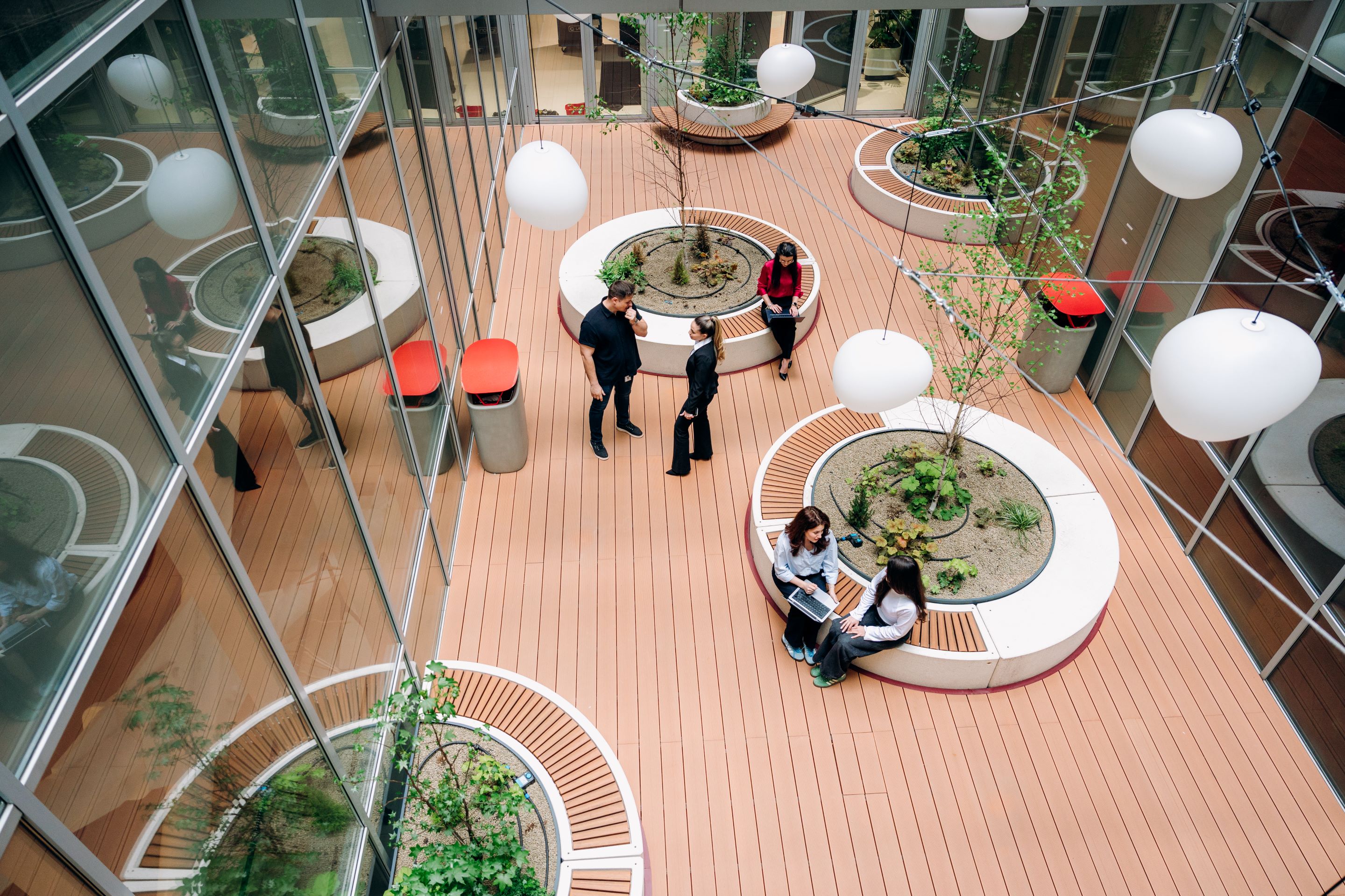 A spacious indoor courtyard featuring plants, seating areas, and people engaged in conversation and work.