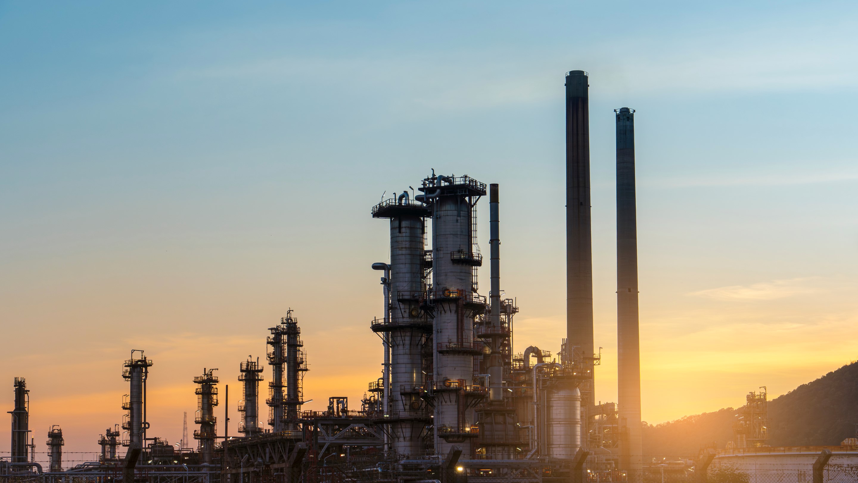  A silhouetted image of an industrial facility at sunset, featuring multiple towers and smoke stacks.