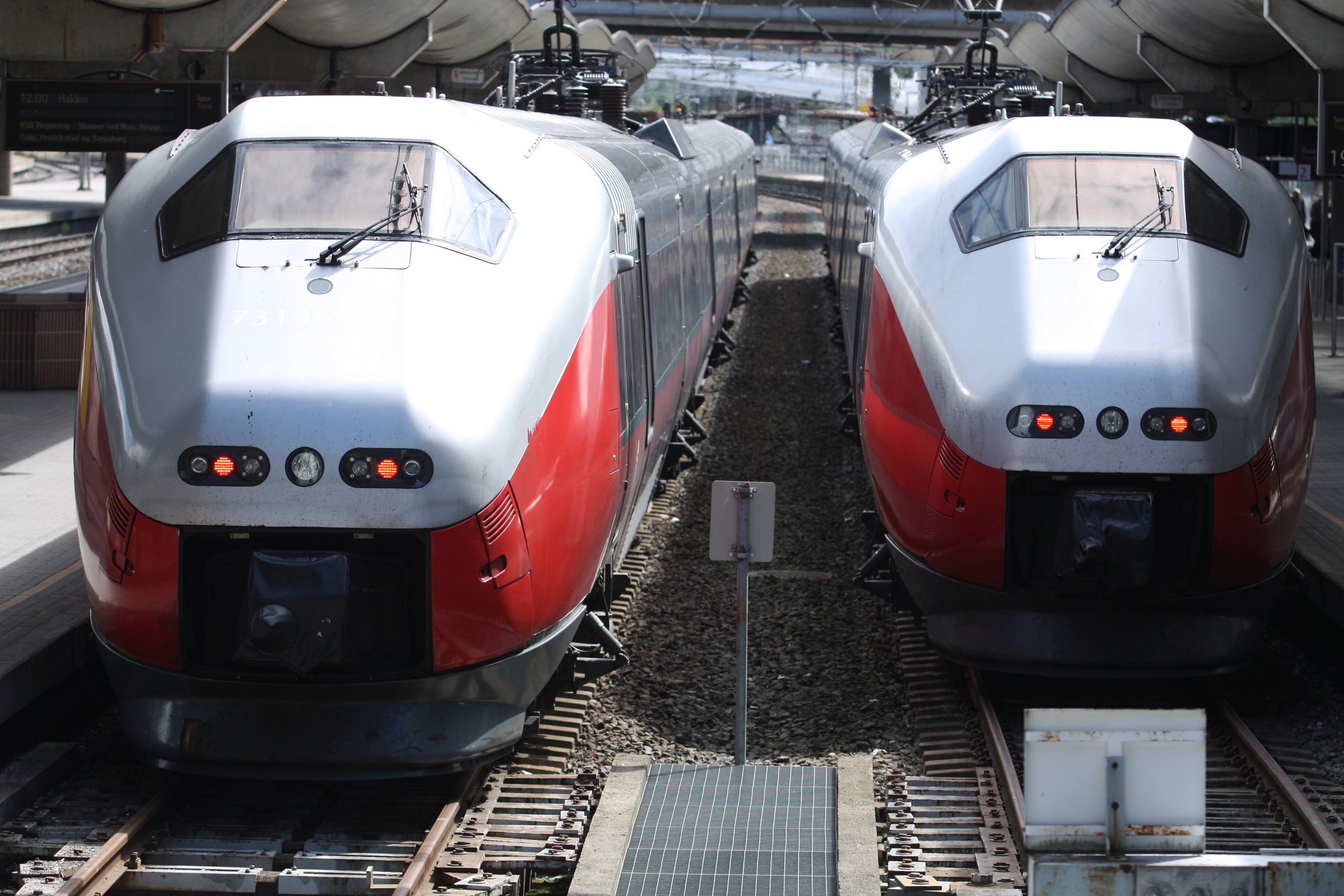 Two modern red and silver electric commuter trains sit side-by-side at a railway station platform.