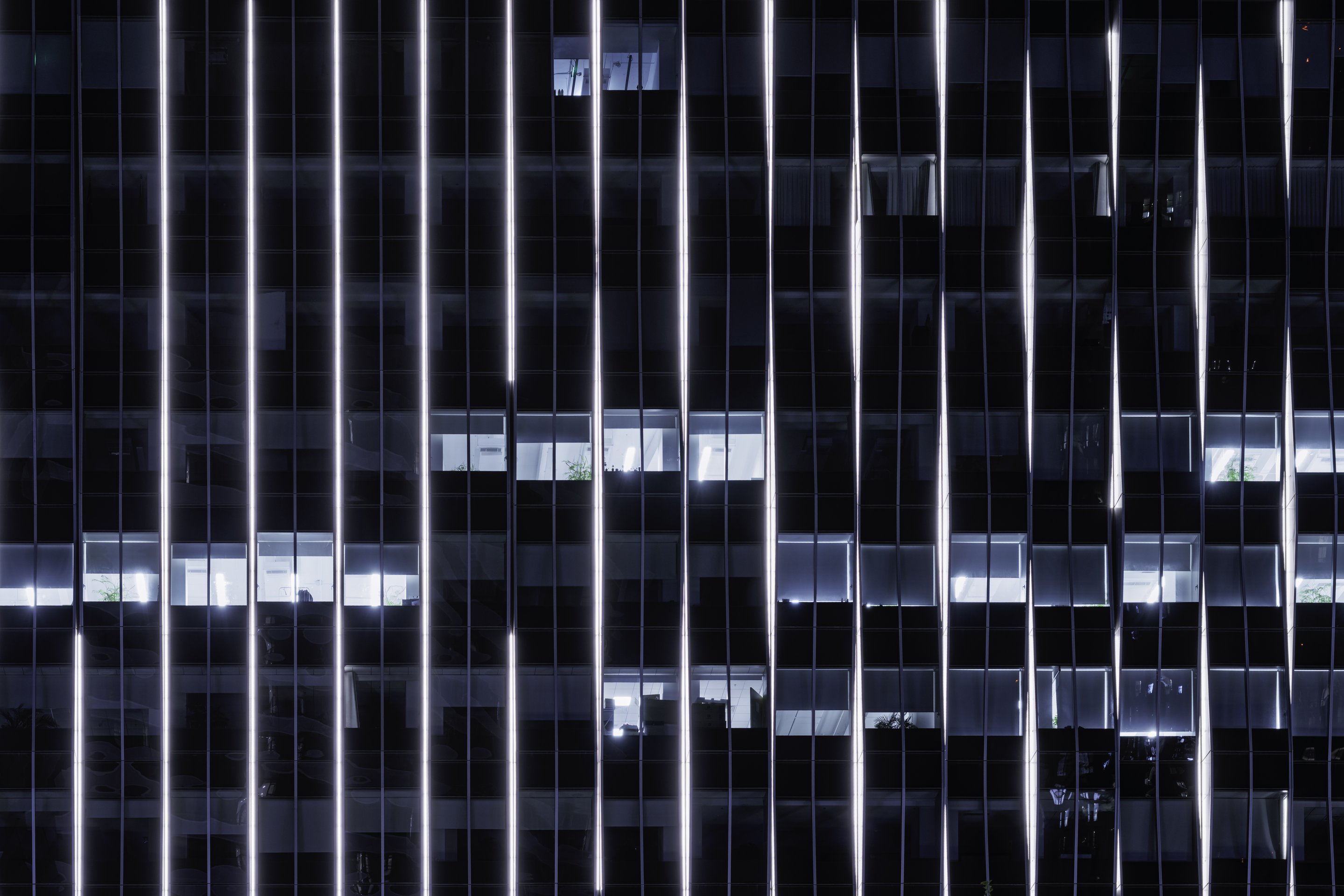 Vertical light strips emphasize the architectural grid of a modern high-rise office building during the night.