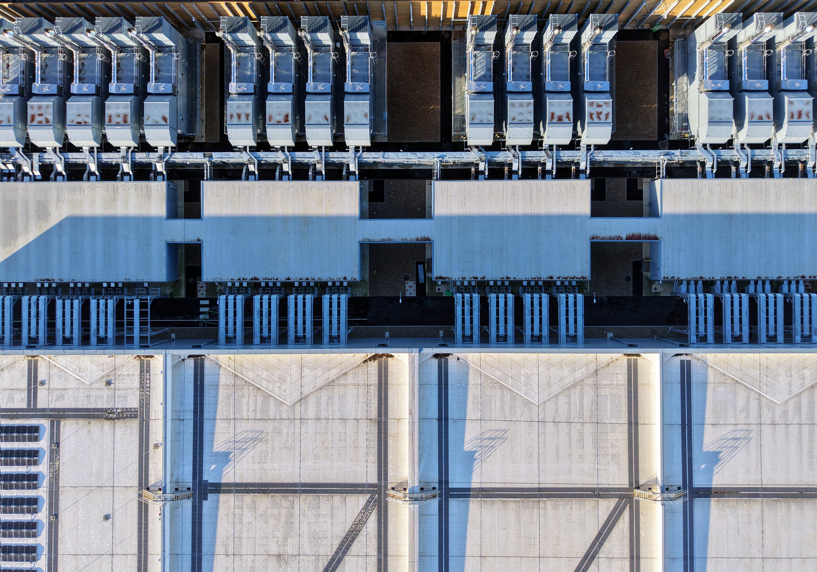 An overhead aerial view of an industrial facility roof featuring modular HVAC cooling units and large structural concrete ventilation segments.