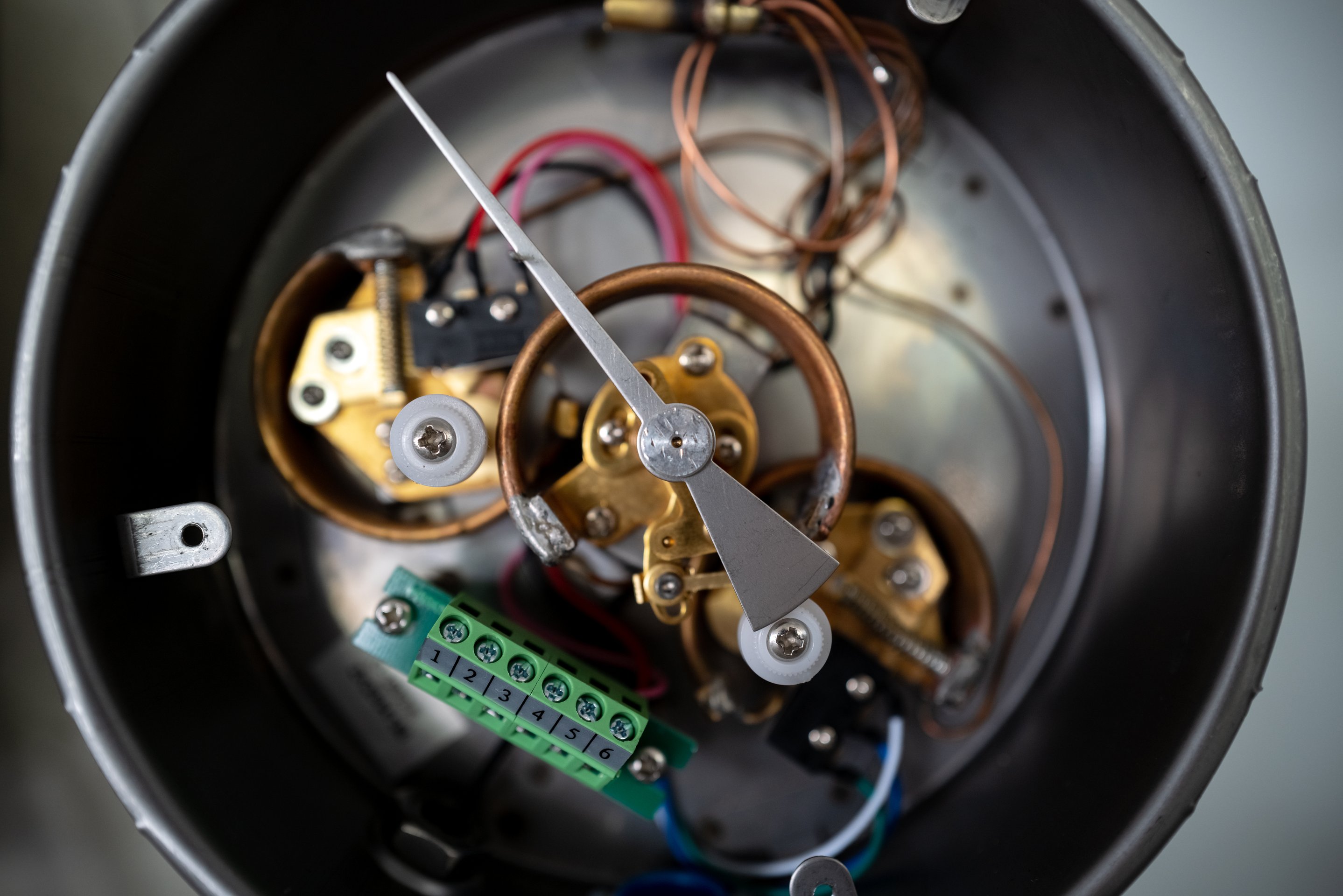 An overhead view reveals the intricate brass gears, wiring, and numbered terminal block inside an open industrial pressure gauge housing.