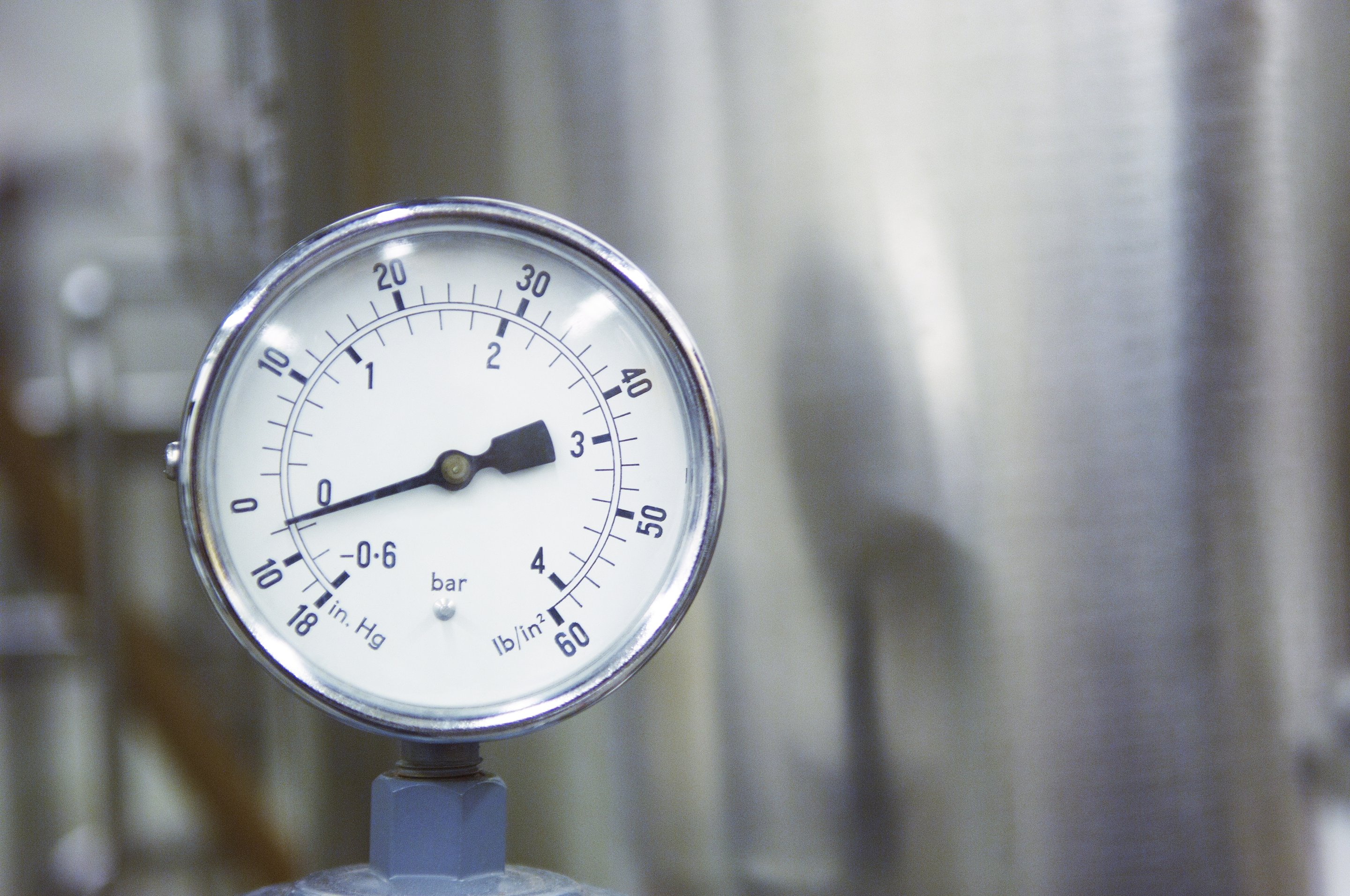 A close-up view of an analog pressure gauge measuring industrial equipment settings in bar and inches of mercury.