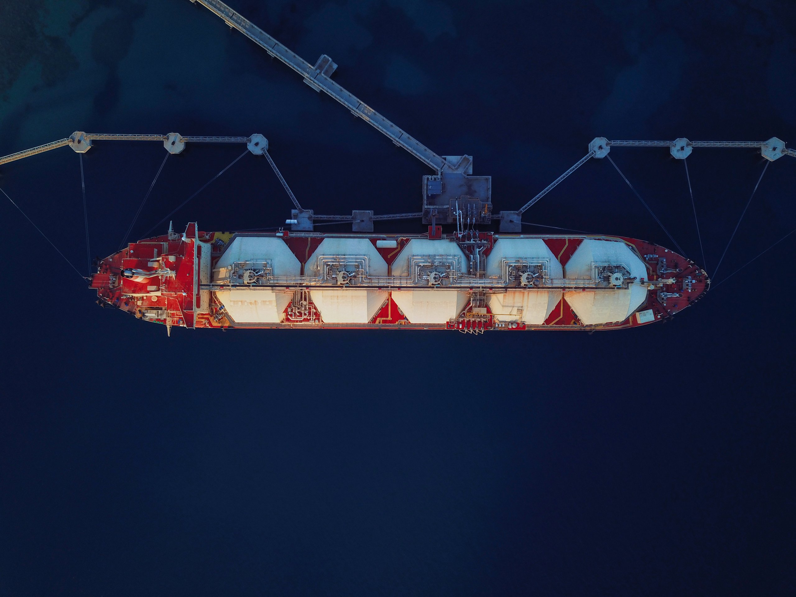 An aerial top-down view of a Liquefied Natural Gas tanker moored at an industrial jetty for cargo offloading operations.