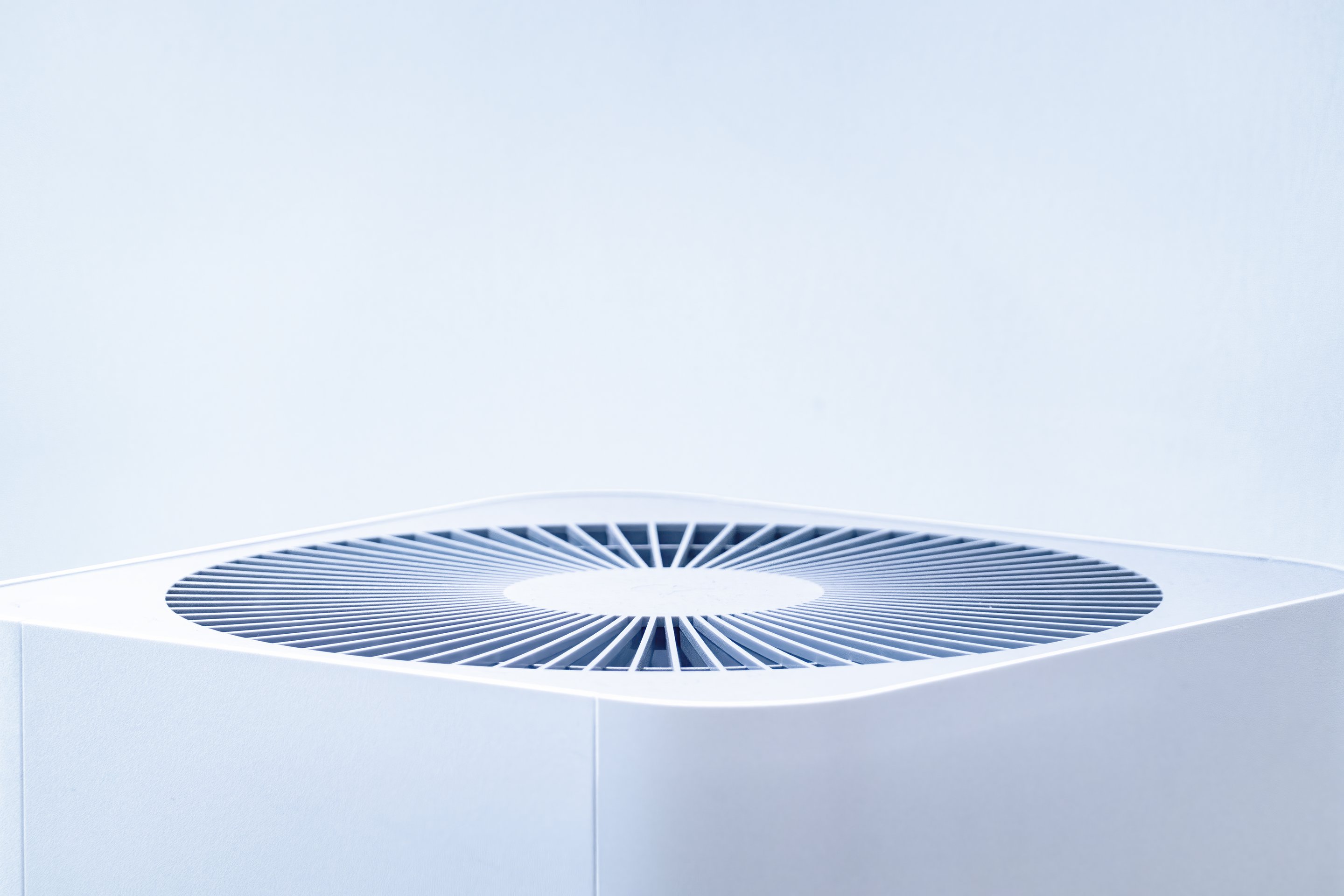 A sleek, white air purifier unit captured against a minimalist light blue background to highlight its contemporary industrial design.