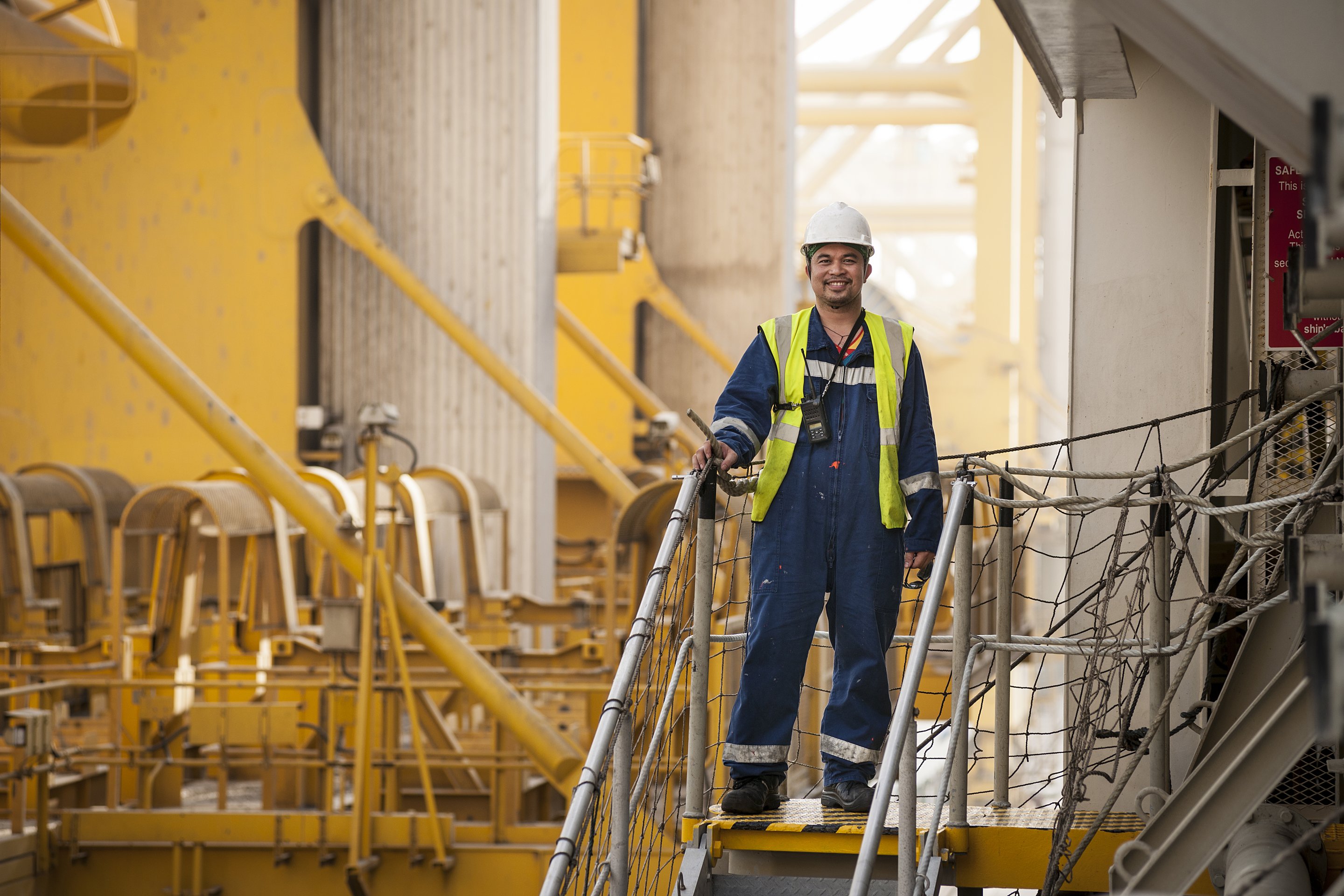 An smiling worker in high-visibility gear stands on an industrial platform.
