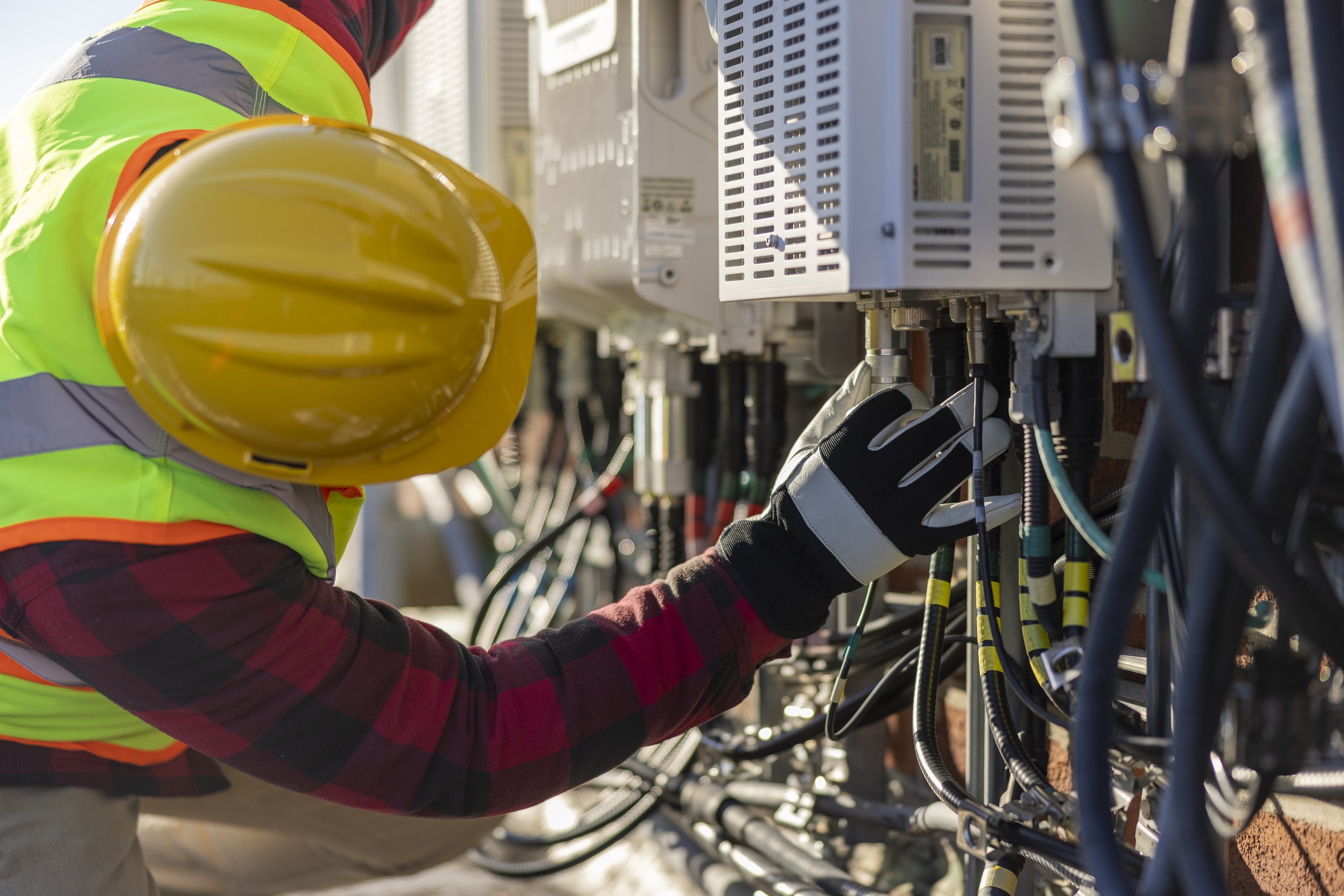 A field technician wearing safety gear connects wiring to industrial electrical equipment during a site installation.