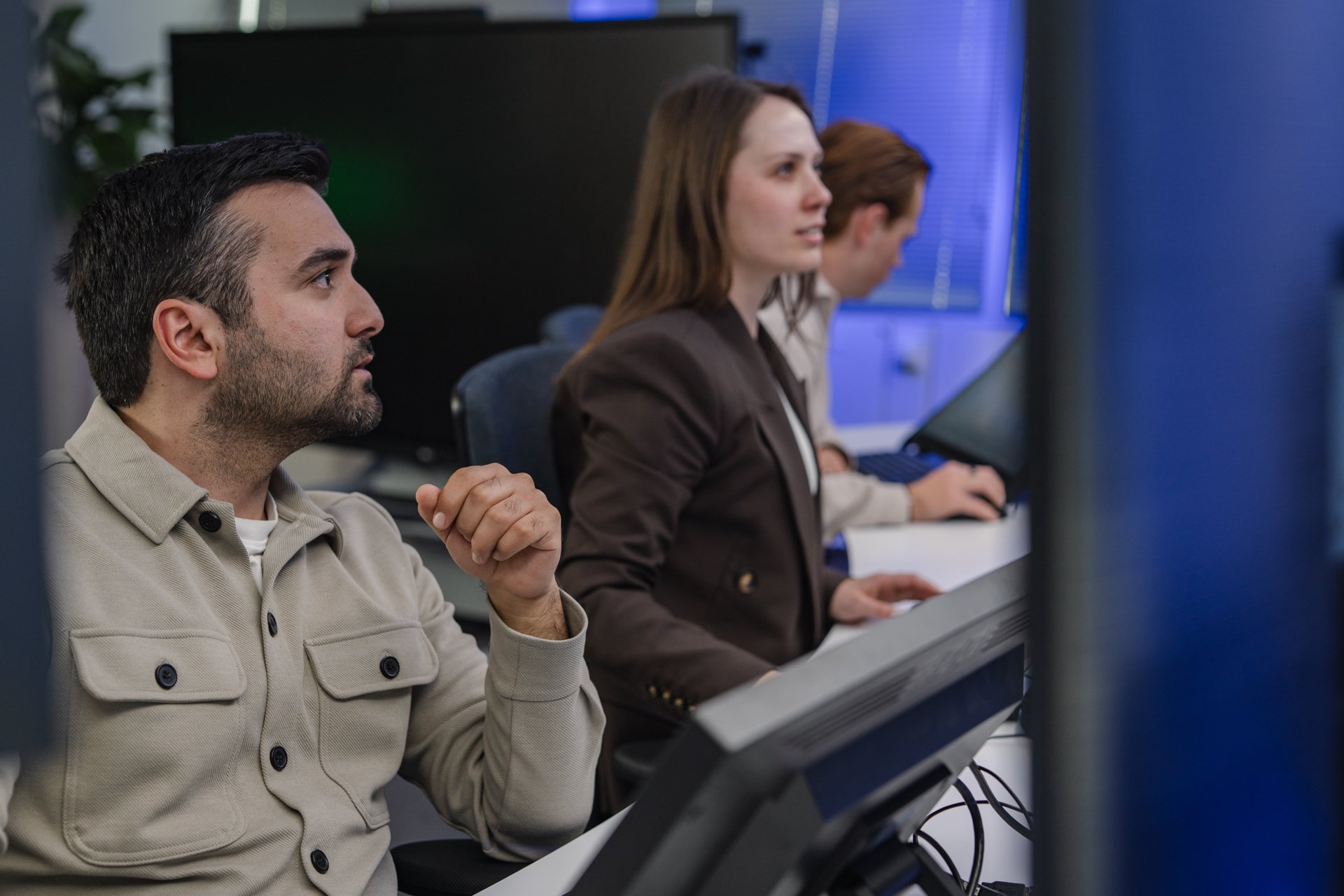 A diverse group of professional colleagues collaborating in a modern office, focused on their workstation monitors for data analysis and operational oversight.