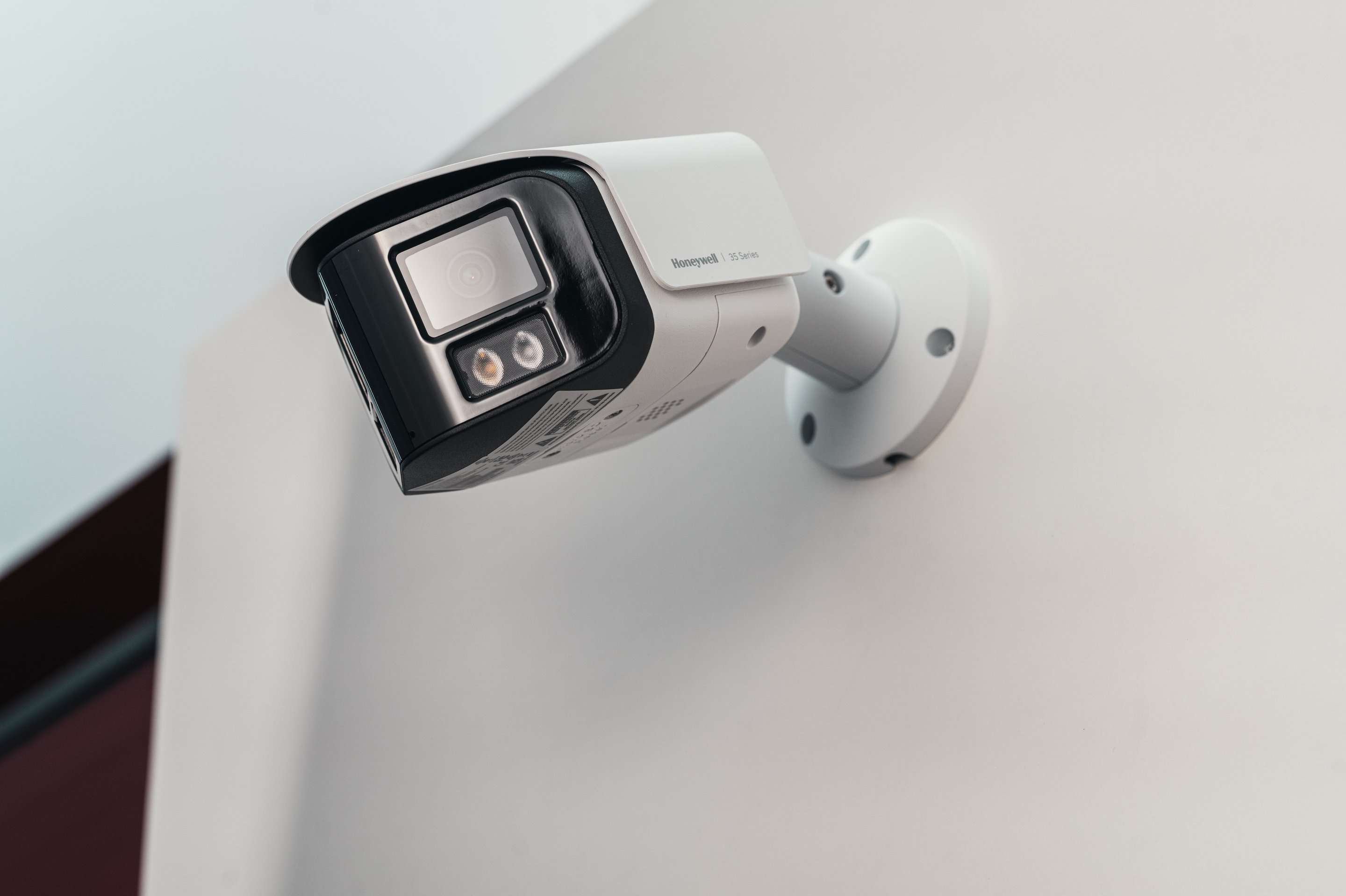 A low-angle shot of a Honeywell 35 Series surveillance camera mounted on a plain white wall for industrial security monitoring.
