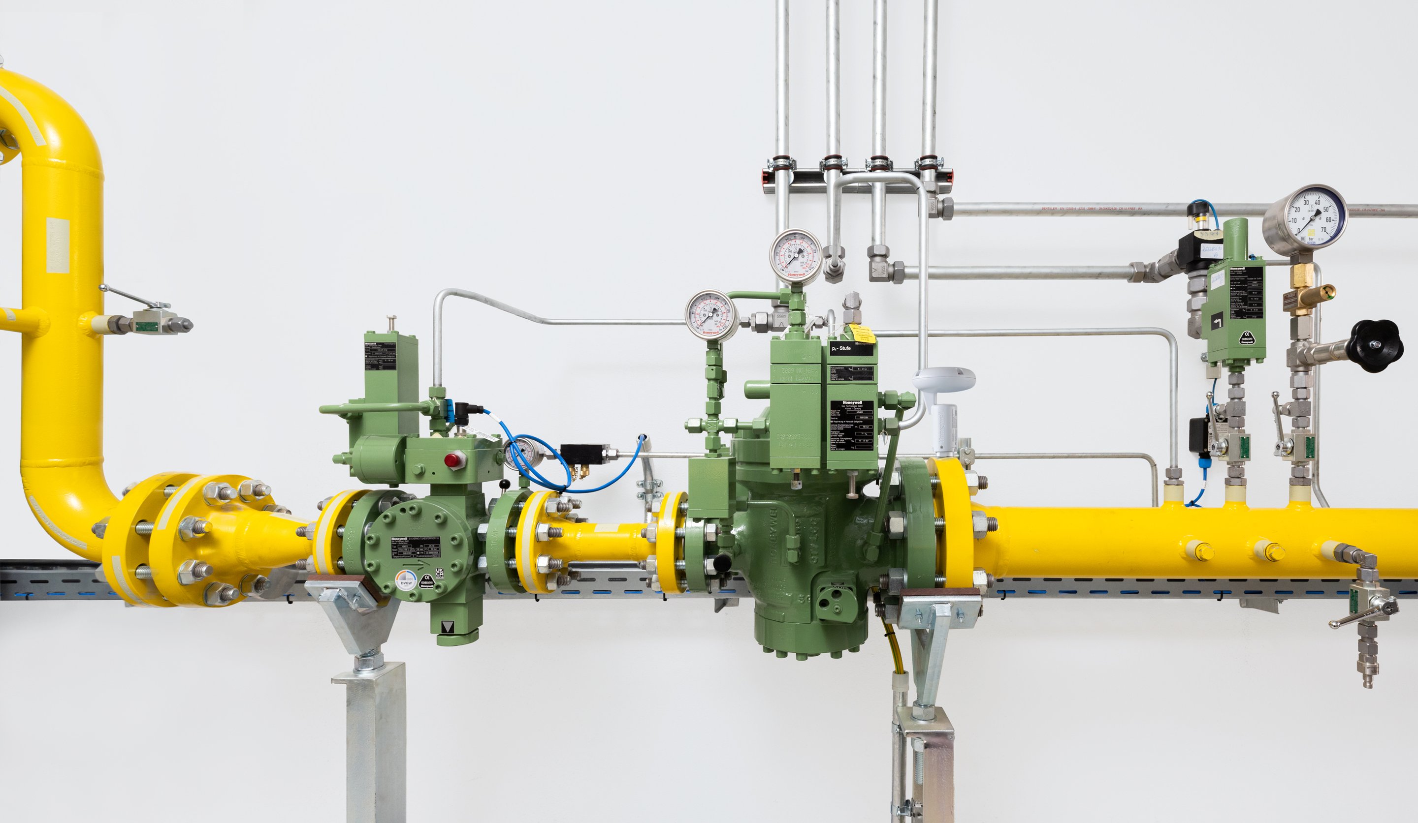 A complex industrial pipeline featuring yellow piping, pressure gauges, and green control valves against a clean white background.