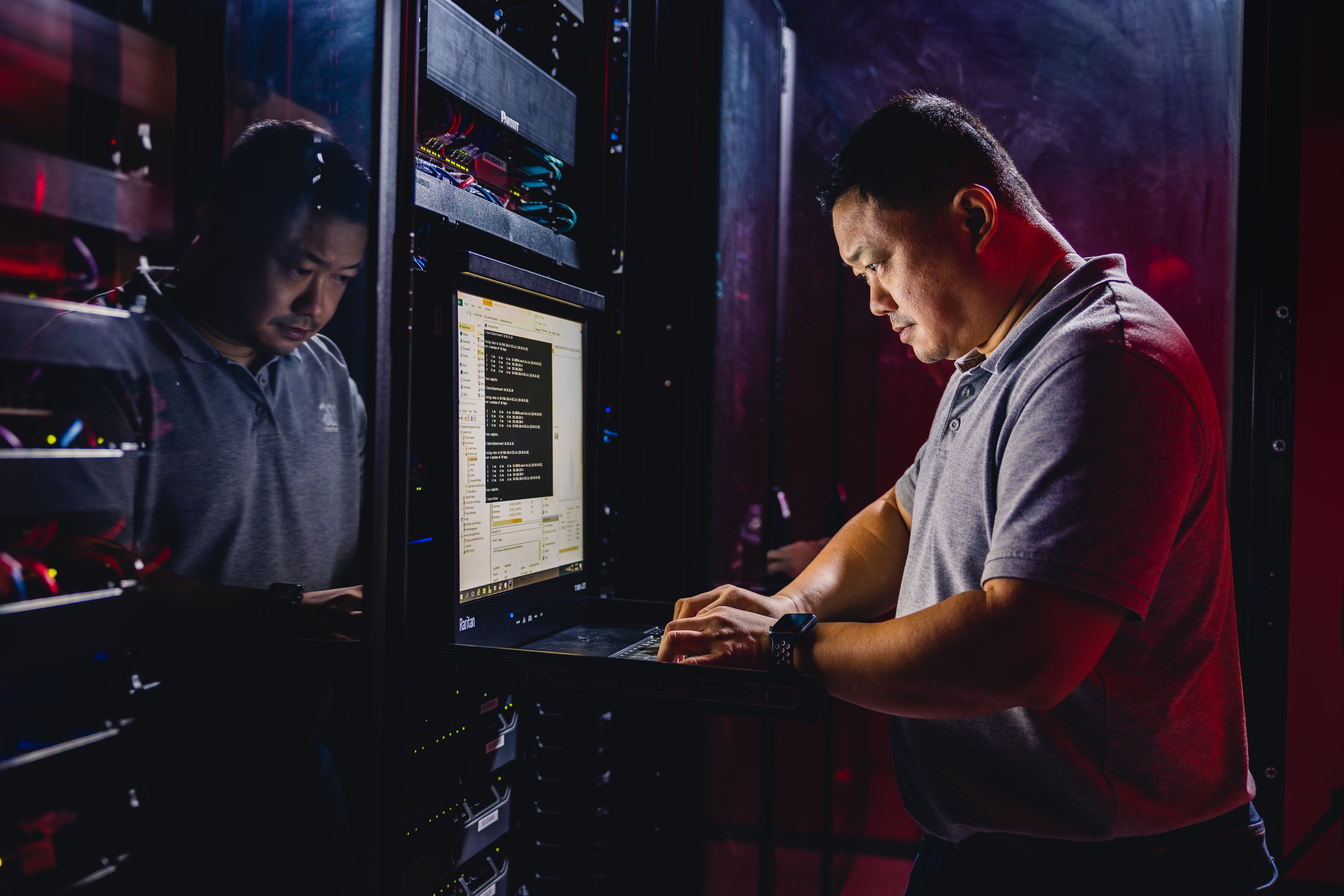A focused technician works on a server rack console within a high-tech data center environment illuminated by atmospheric red and blue lighting.