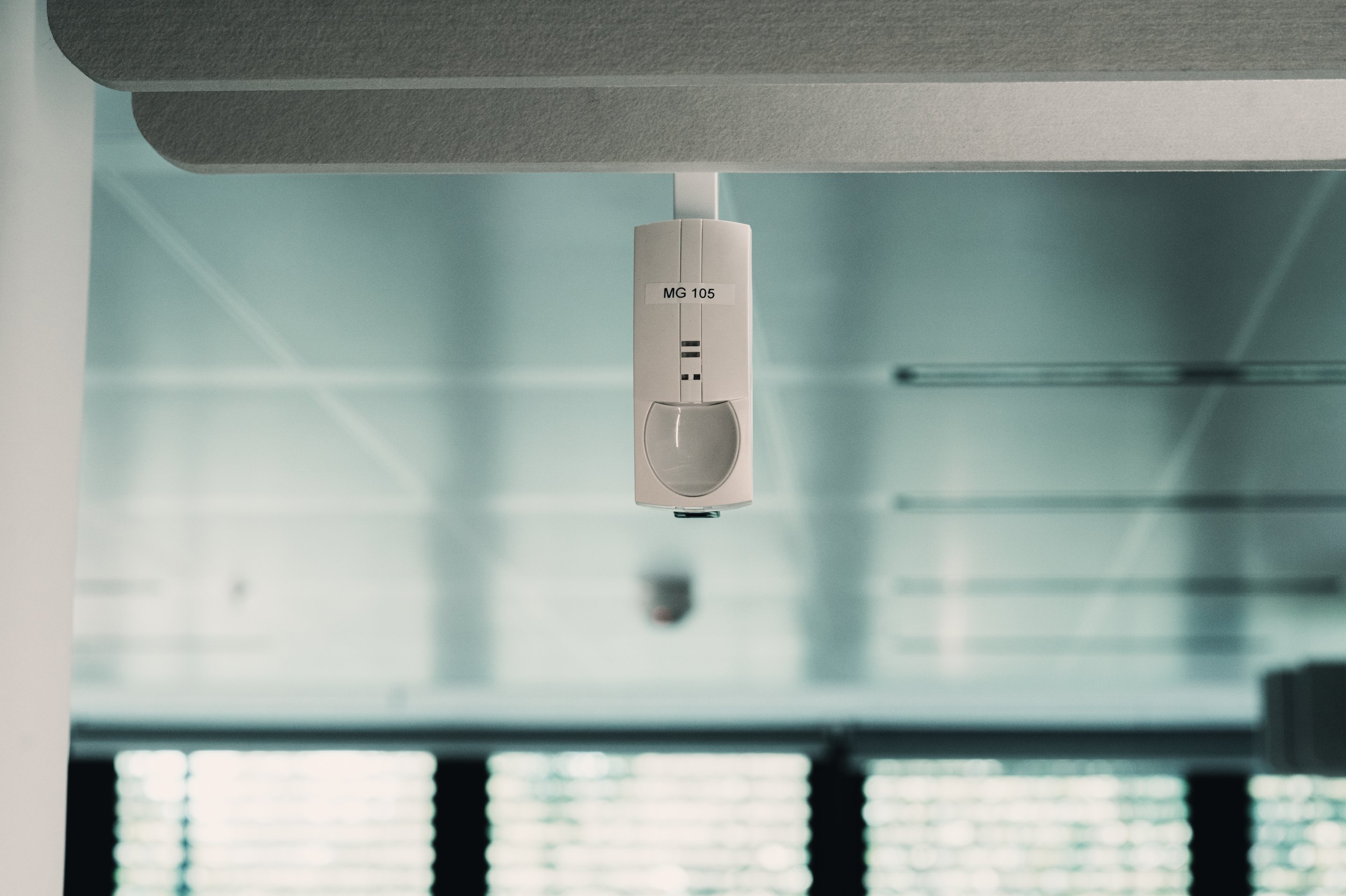 An indoor ceiling-mounted motion sensor labeled MG 105 installed in a modern office environment.