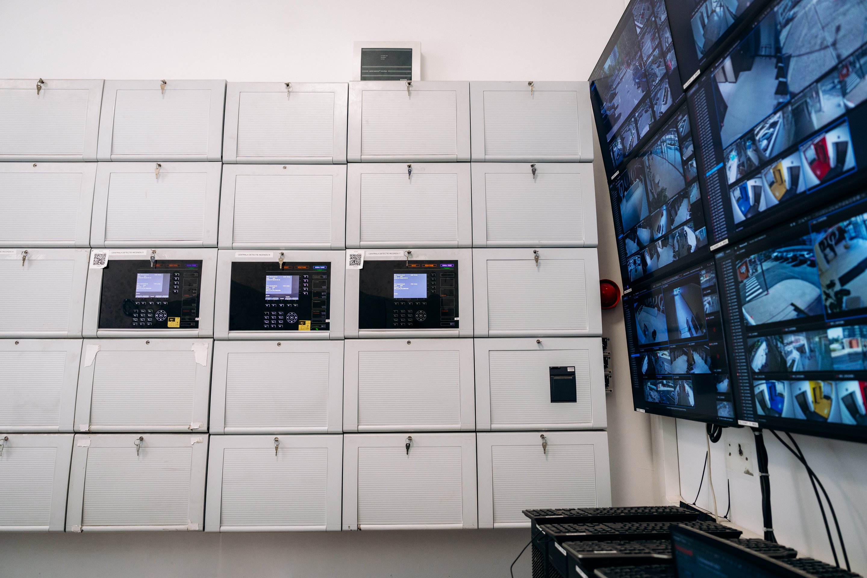 Monitoring station with wall-mounted fire alarm panels and multiple CCTV screens.