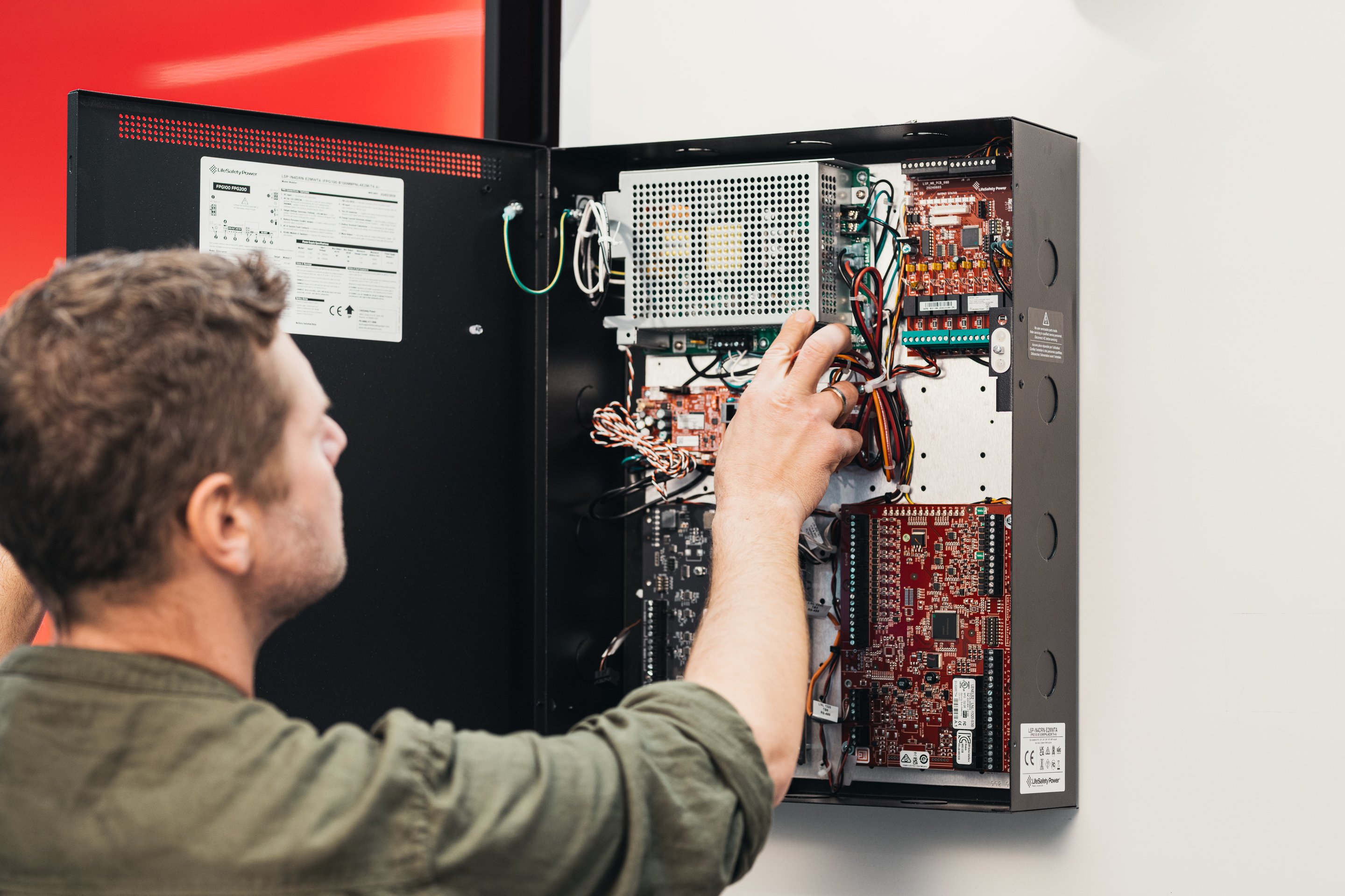 A professional technician performs maintenance and wiring adjustments on an industrial power supply and control circuit board.