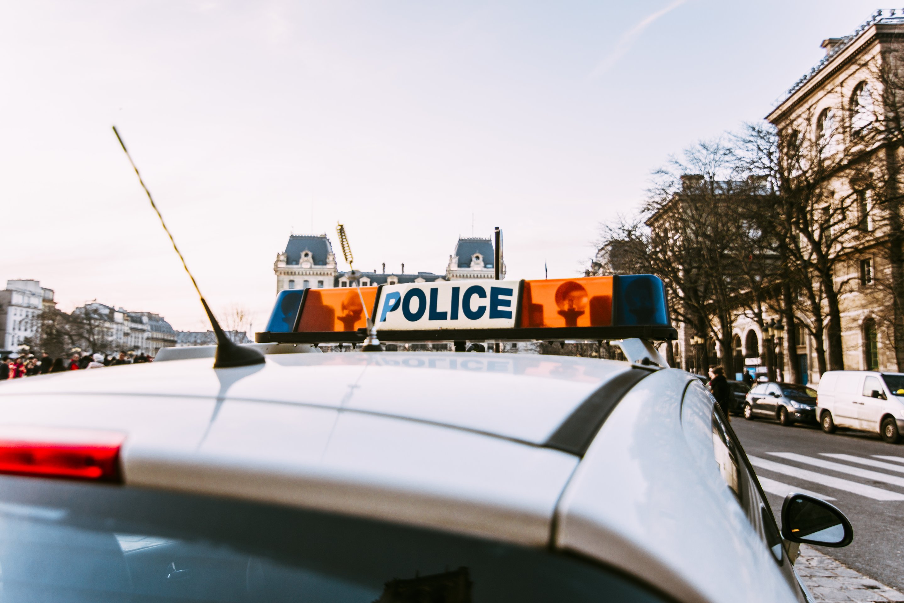 A low-angle rear view of a police car roof light bar parked on a city street during the day.