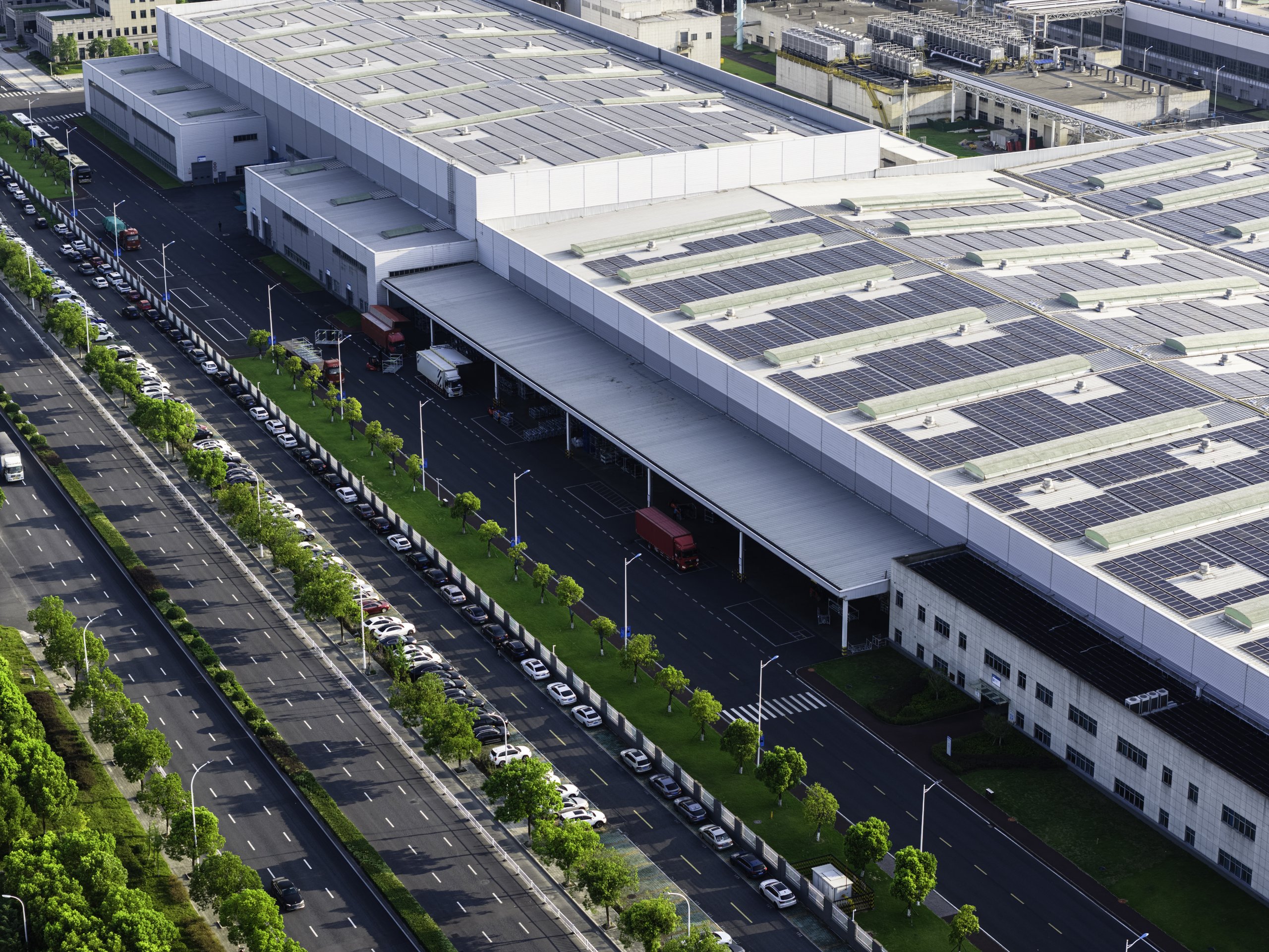 An aerial view of a large warehouse complex featuring extensive roof-mounted solar panels and a busy parking and loading area.