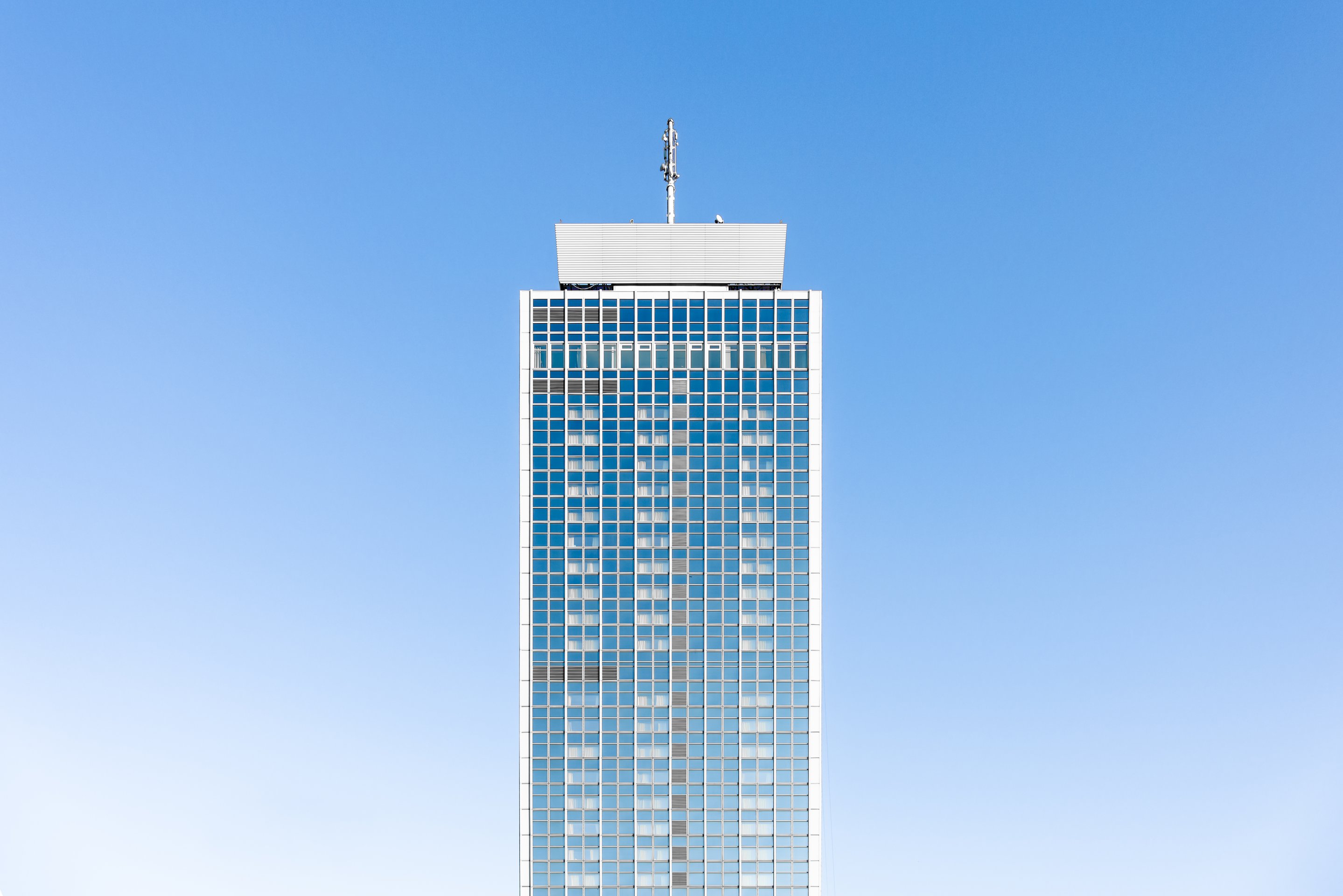 A minimalist architectural shot of a modern high-rise building facade featuring a grid of reflective windows against a clear blue sky.