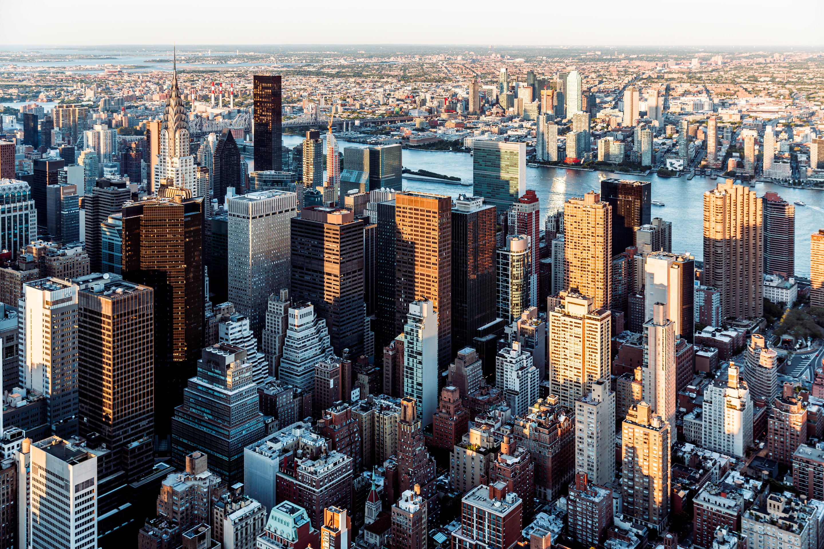 An elevated aerial view captures the sunlit midtown Manhattan skyline and East River during the vibrant golden hour.