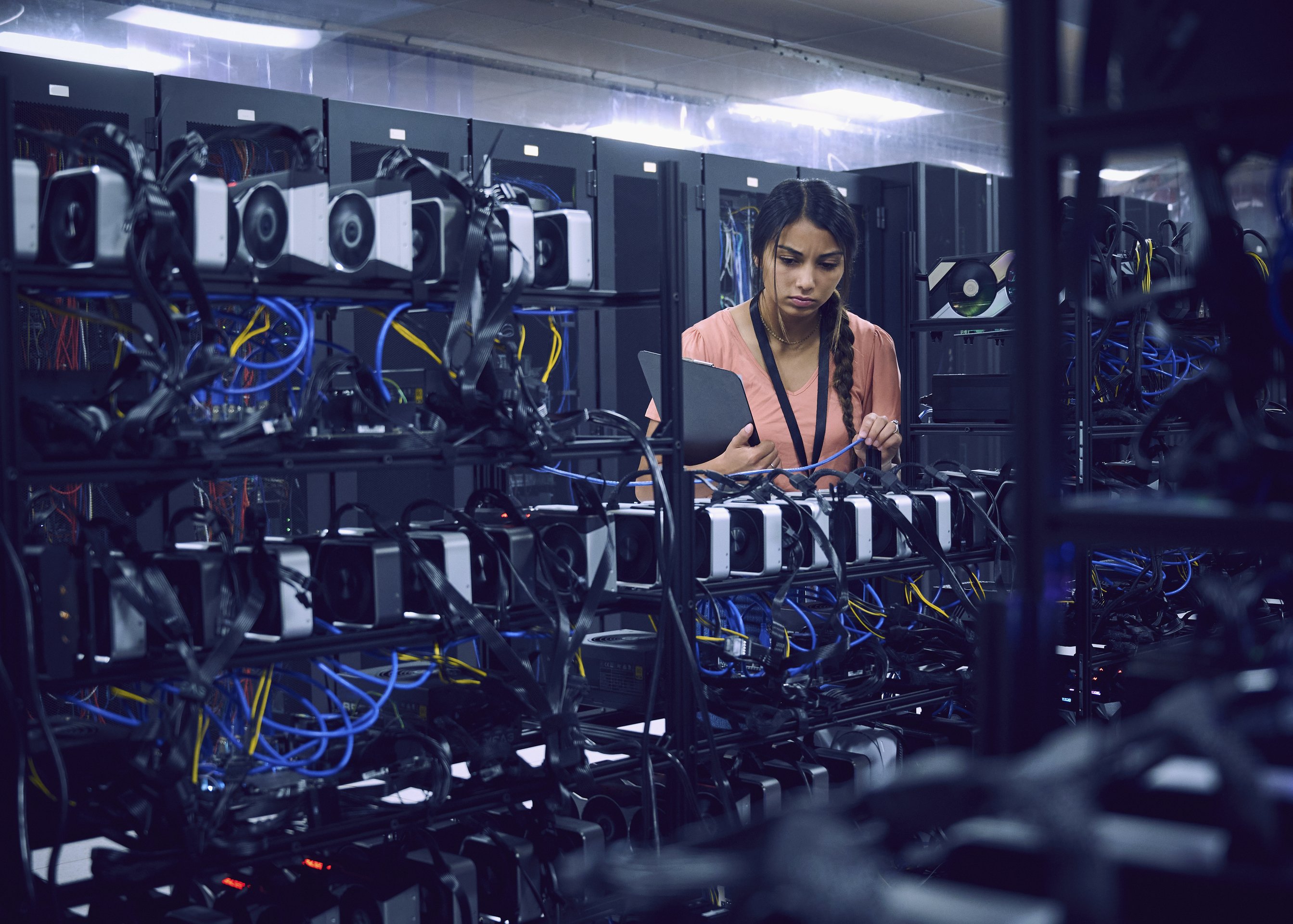 A focused technician inspects cable connections on high-performance server racks within a modern data center facility.