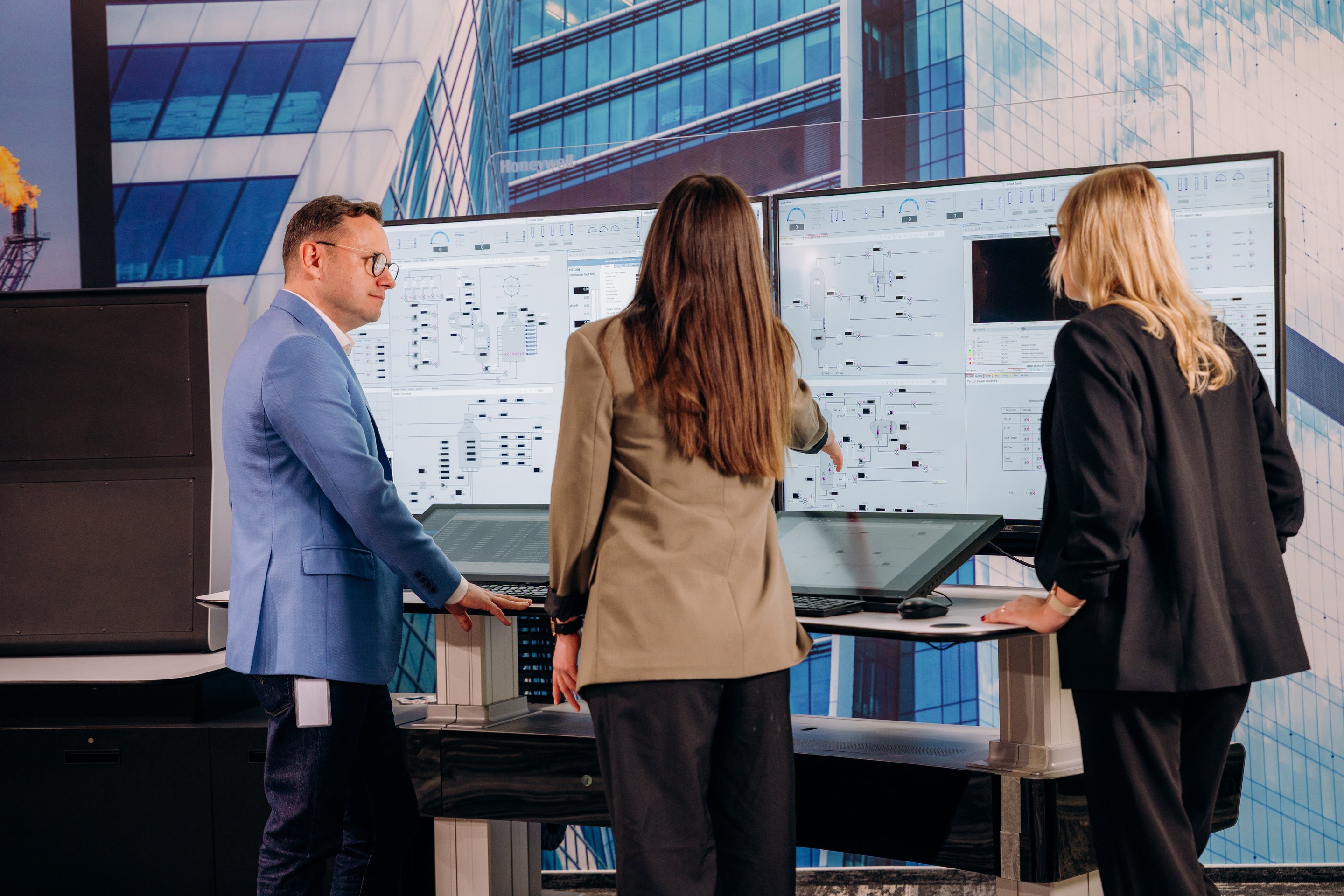 Professionals analyze complex industrial data displayed on large digital monitors in a modern control room environment.