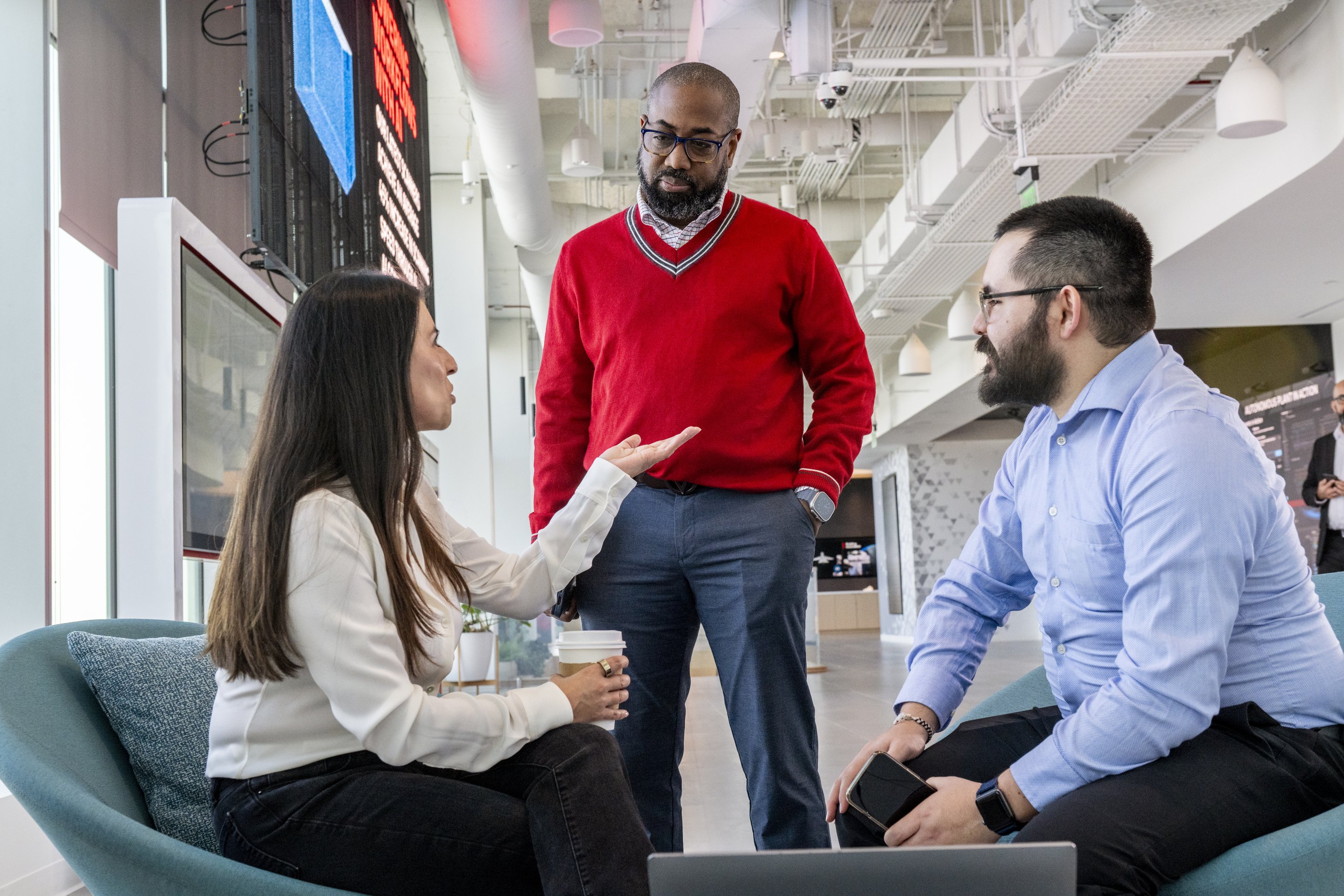 A diverse group of three professionals engages in a collaborative discussion within a modern, open-concept office workspace.