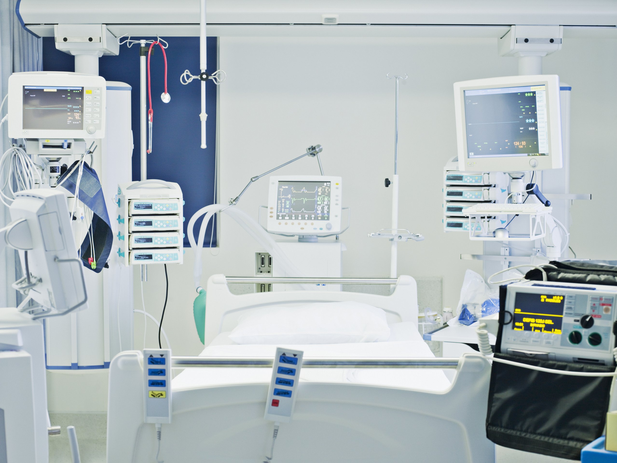 A clean hospital room featuring a high-tech patient bed surrounded by advanced medical monitoring equipment and life-support systems.