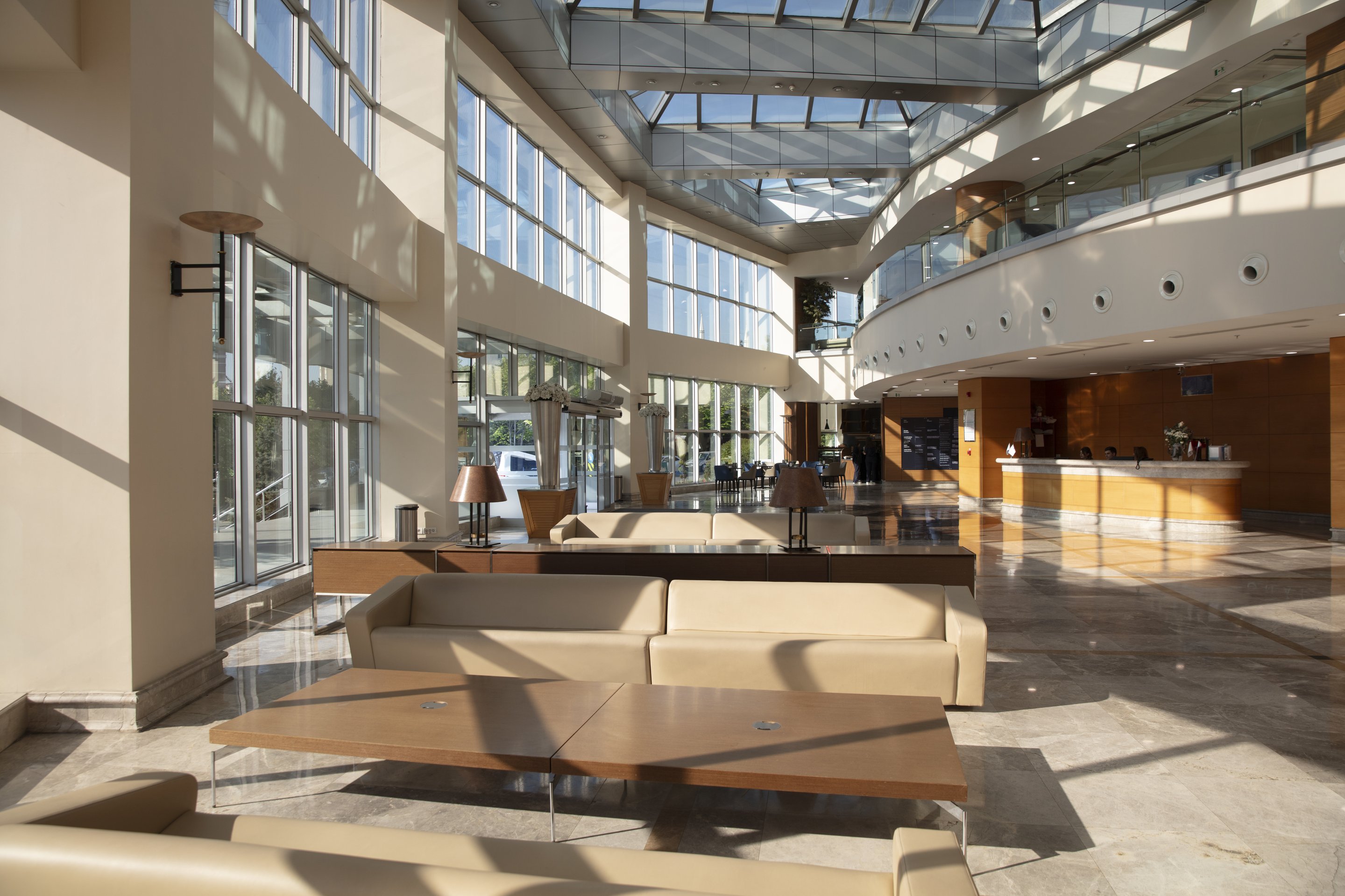 A sunlit, high-ceilinged corporate office lobby featuring modern furniture and glass atrium architecture.