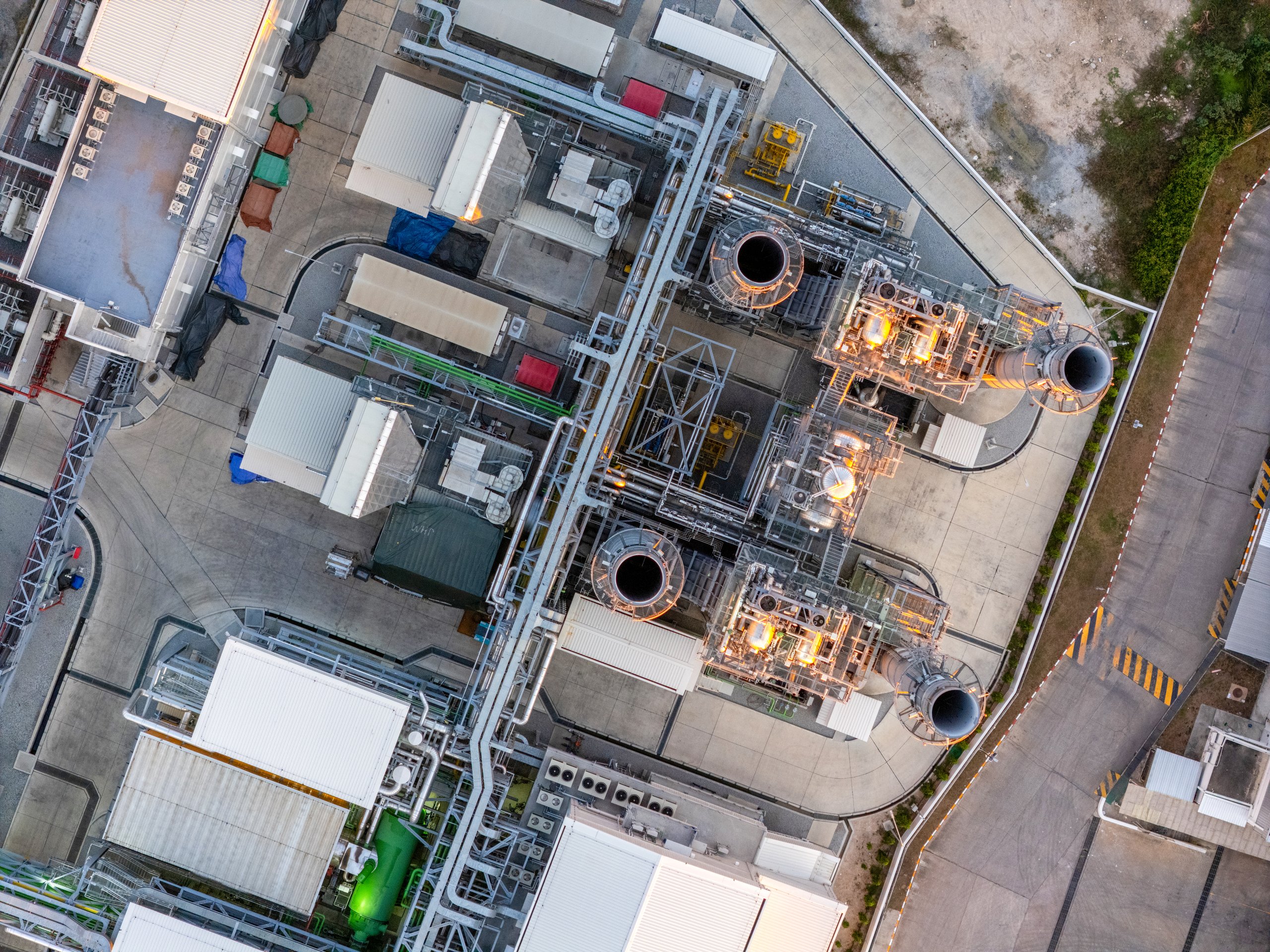 An aerial view captures the intricate machinery and operational exhaust stacks of a modern power plant during the golden hour.