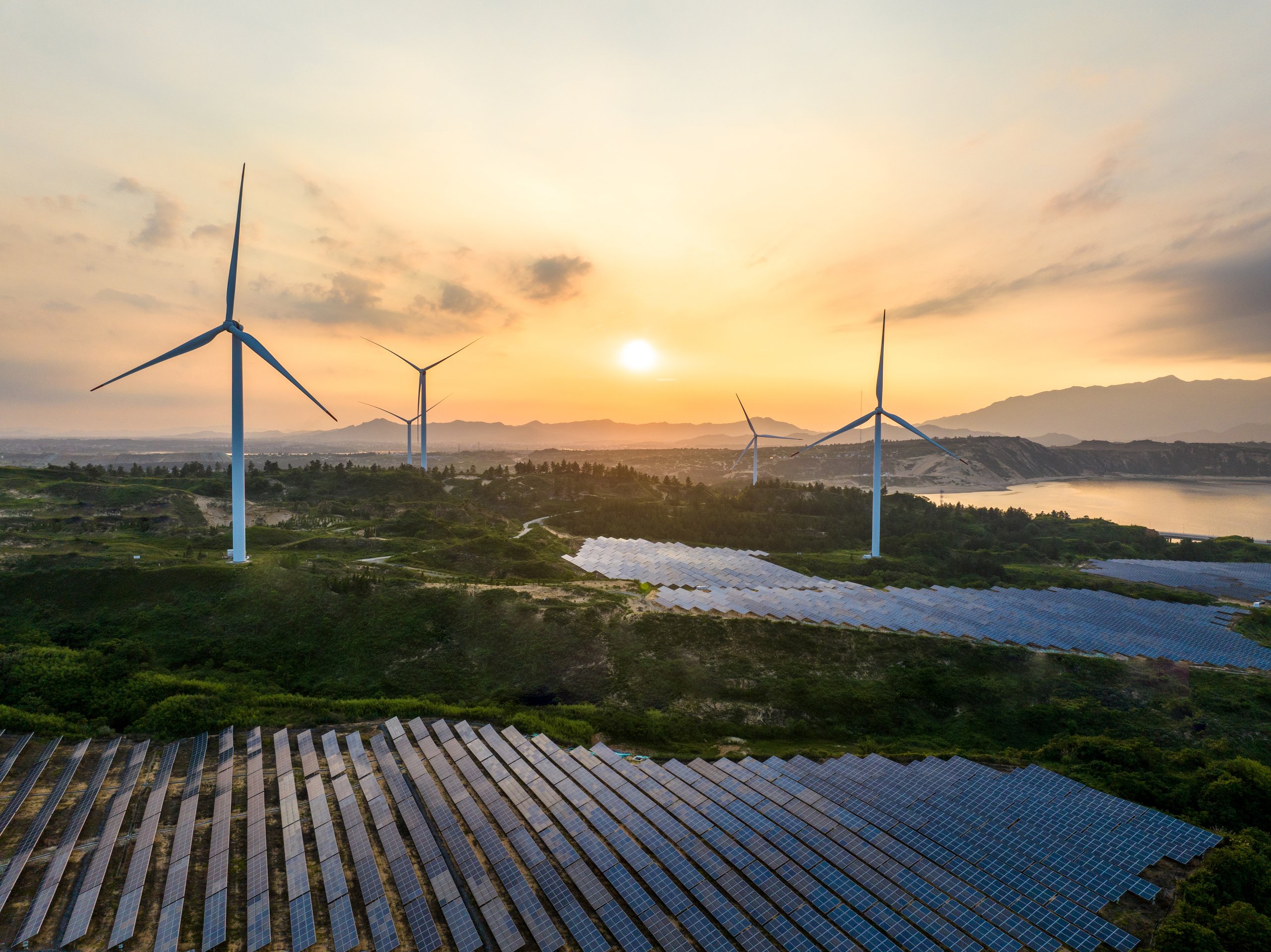 Aerial view of wind turbines and solar panels integrated into a scenic landscape at sunset.