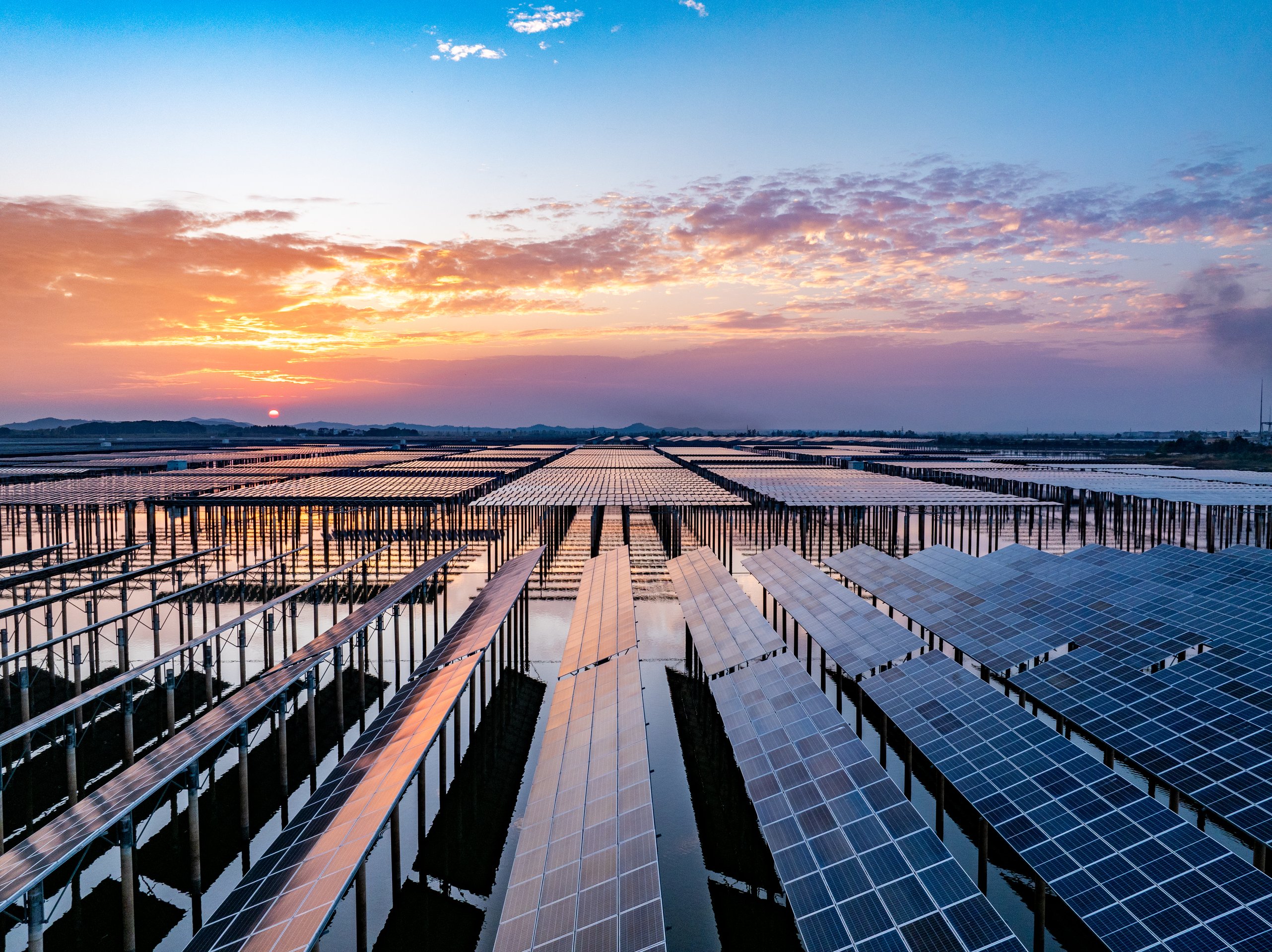 A vast array of floating solar panels stretches across a calm reservoir at sunset, showcasing large-scale renewable energy infrastructure.