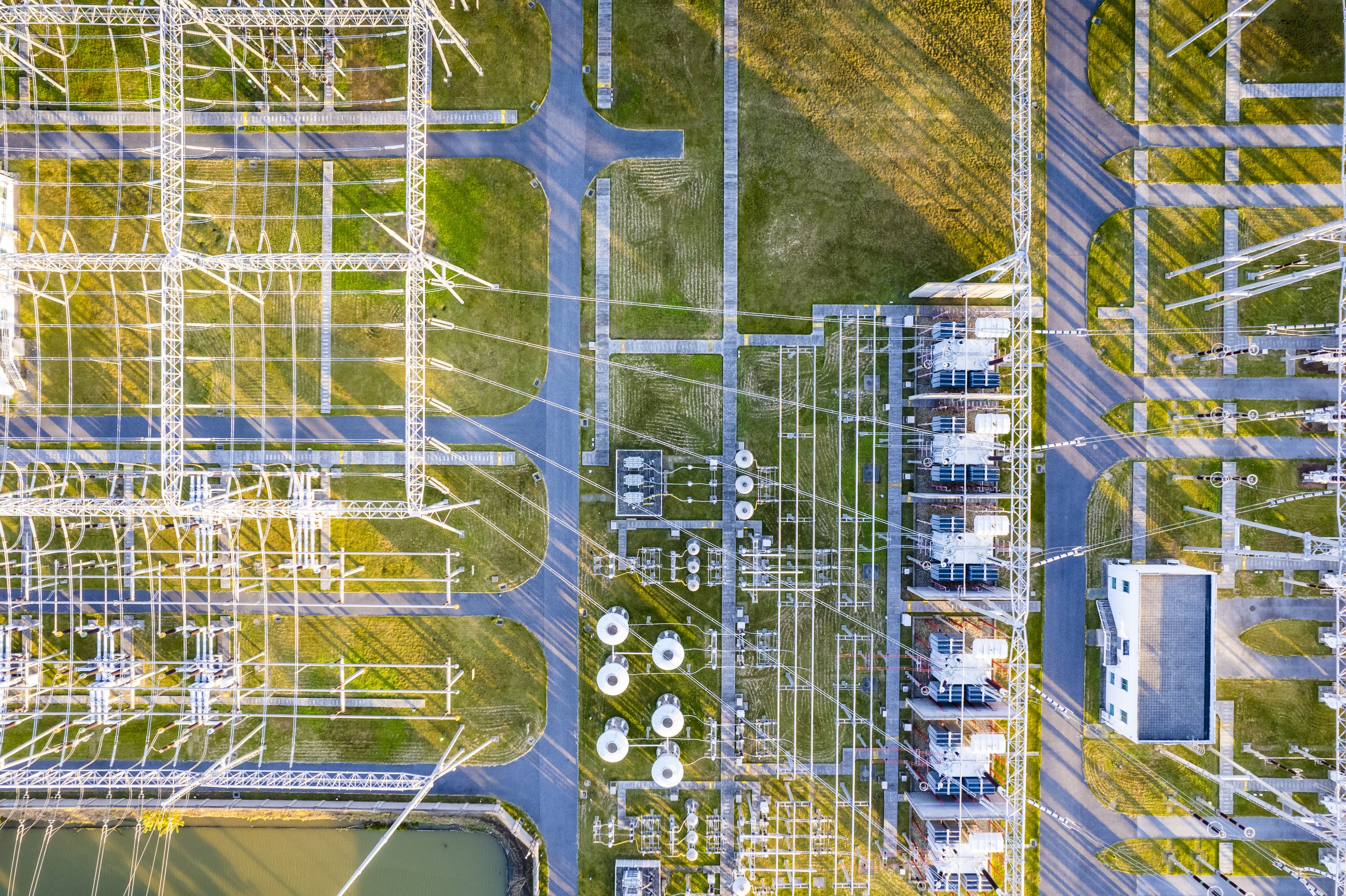 An aerial top-down view of an electrical substation showcasing transformers, intricate wiring, and power transmission infrastructure at golden hour.