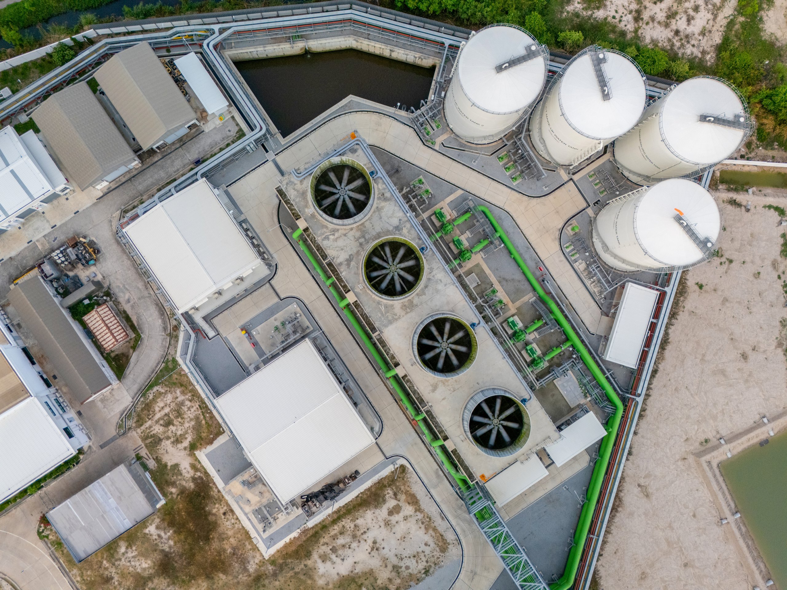 An aerial top-down view shows the cooling towers, storage tanks, and interconnected piping infrastructure of a modern industrial complex.