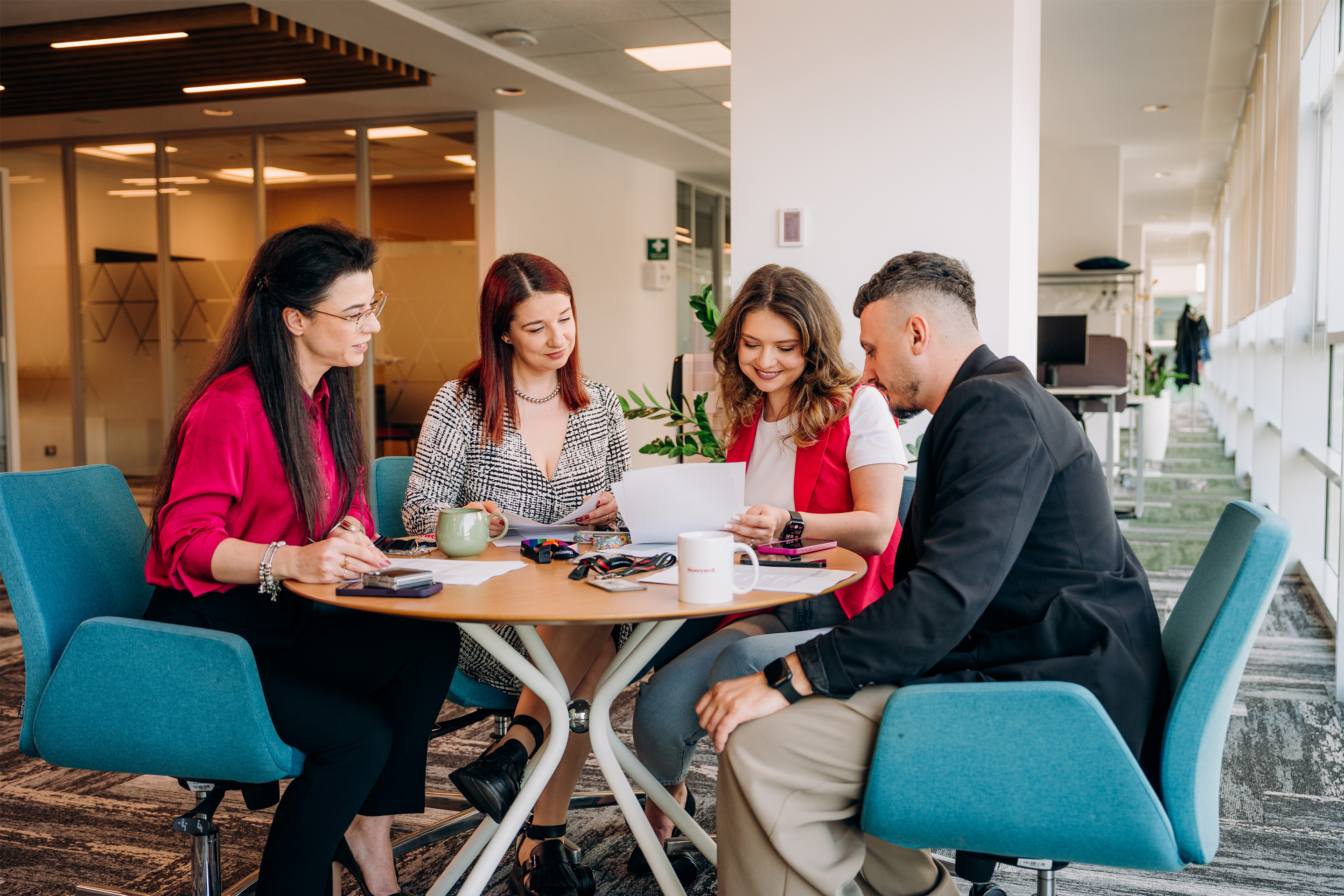 Employees in a modern office collaborate around a table, reviewing documents and discussing ideas—capturing teamwork, productivity, and a dynamic workplace environment.