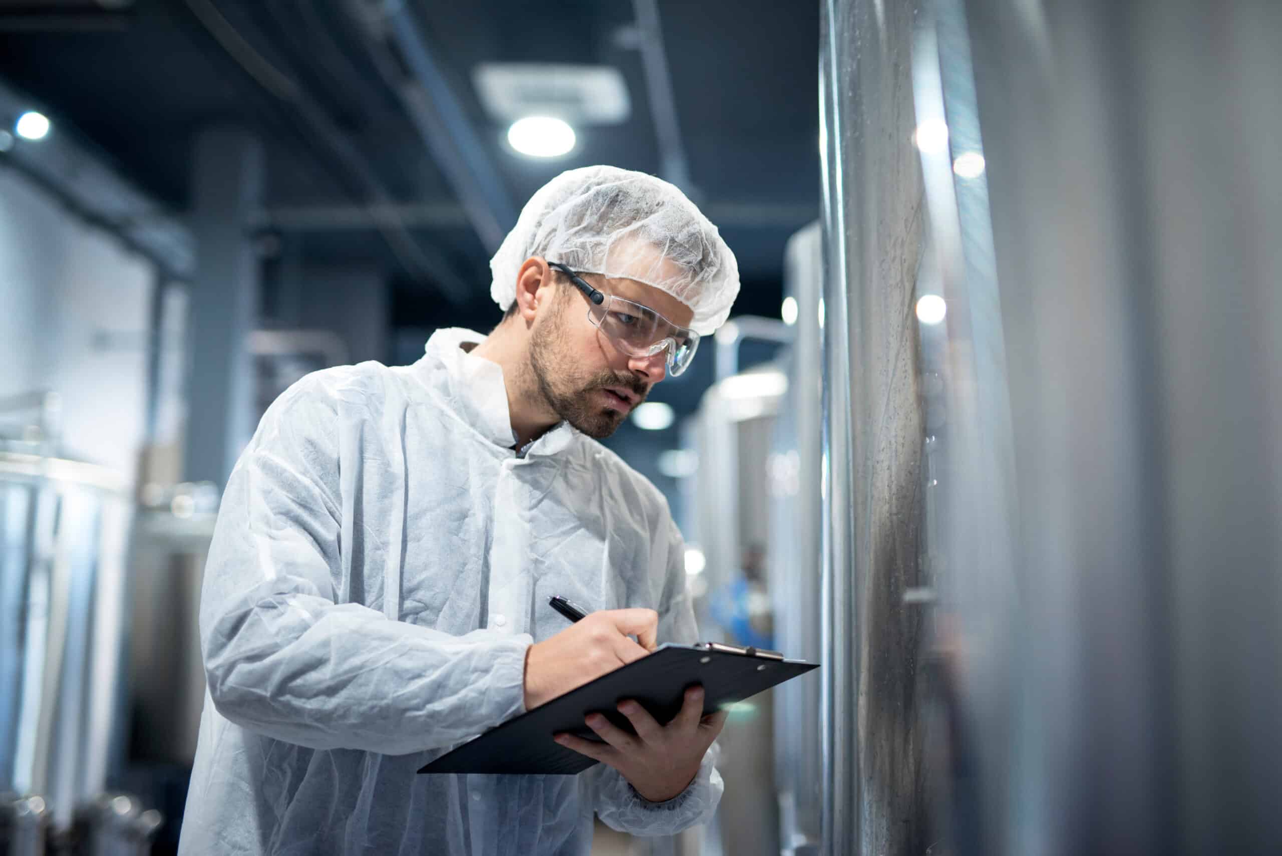 Professional technologist in white protective uniform controlling industrial process at production plant.