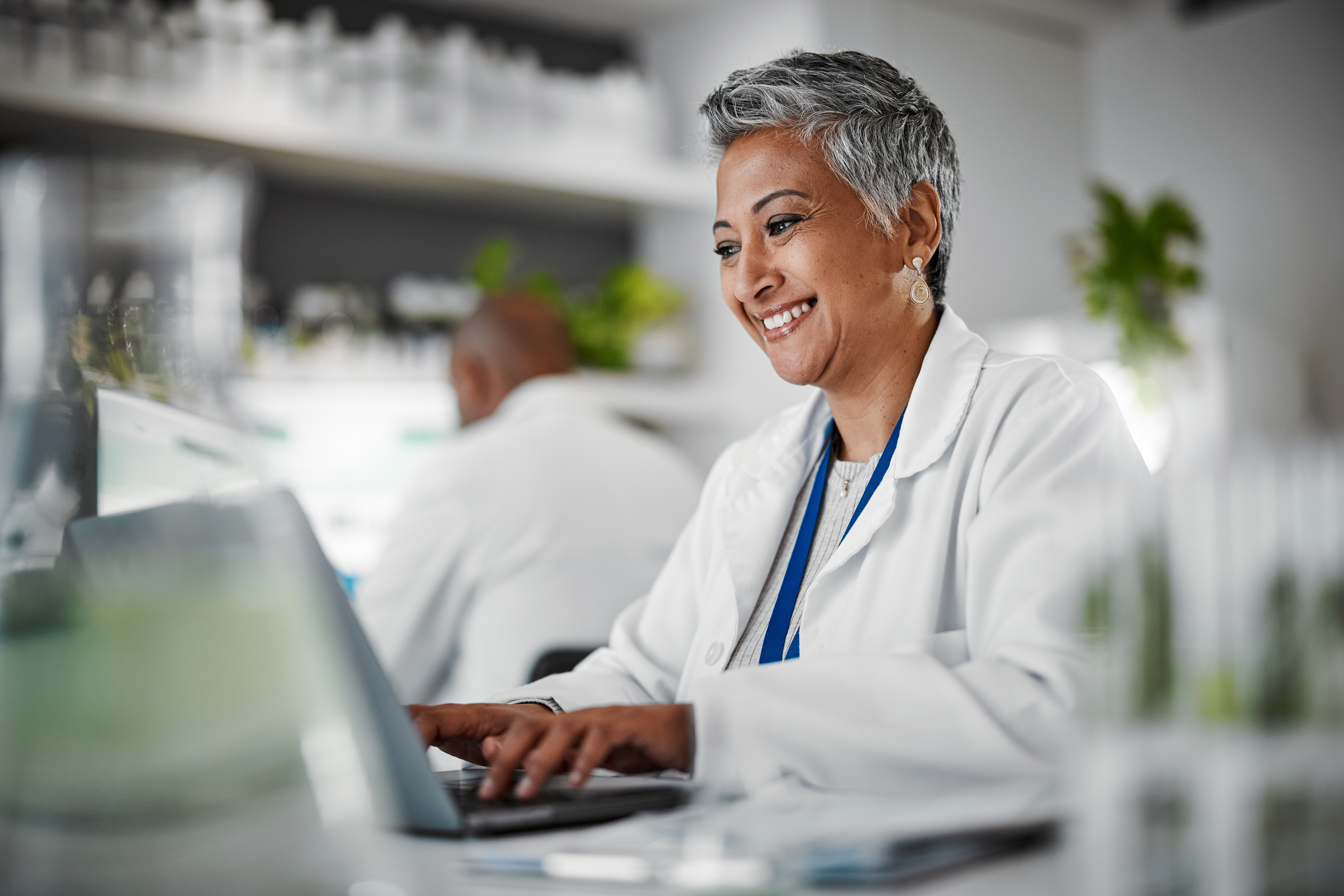 Scientist, senior woman and lab with laptop, research and plants with analytics, pharmaceutical study and focus. Elderly science expert, computer and typing for data analysis for goal in laboratory.