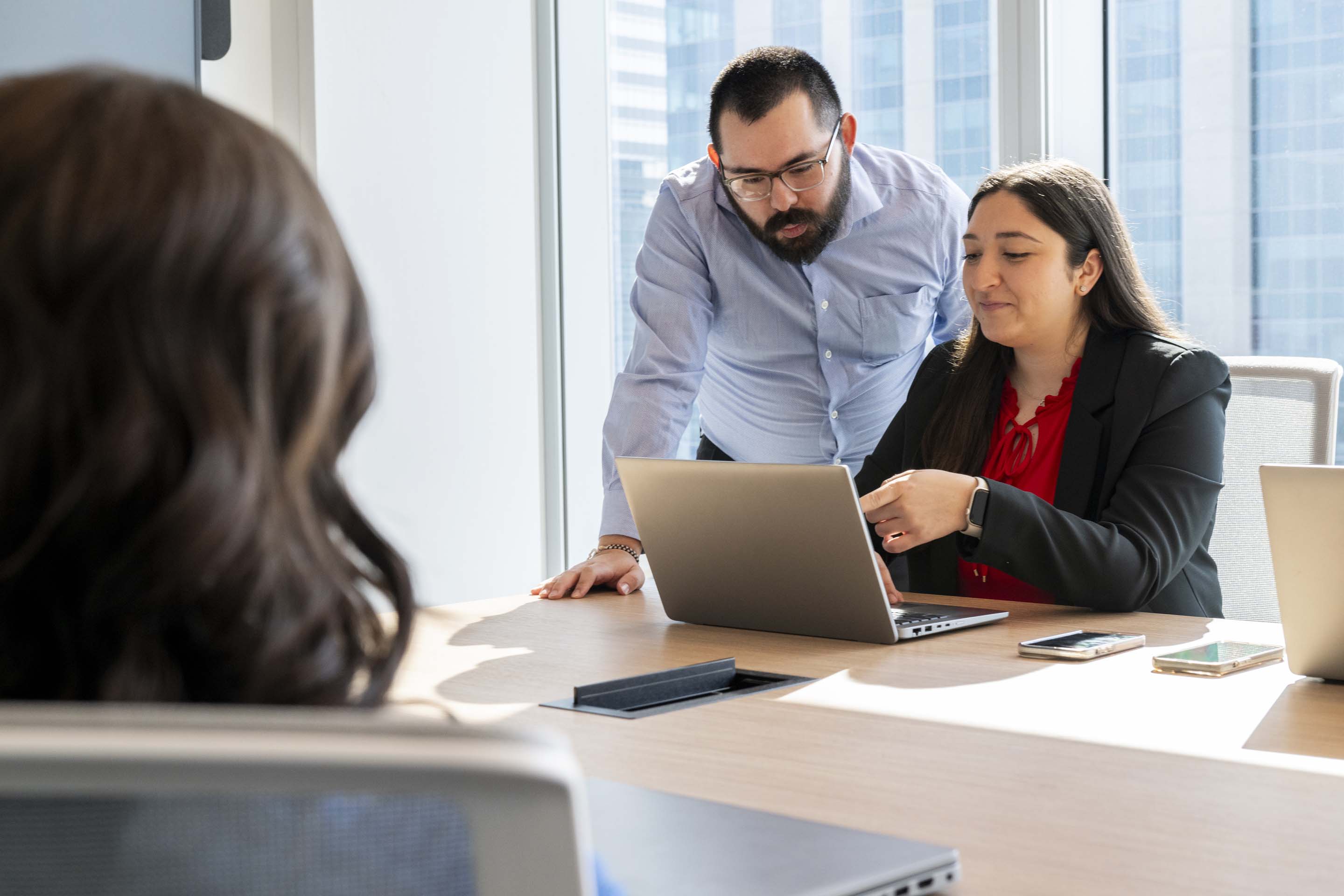 Colleagues working together on a laptop in a professional office environment, representing mentorship, knowledge sharing, and teamwork.