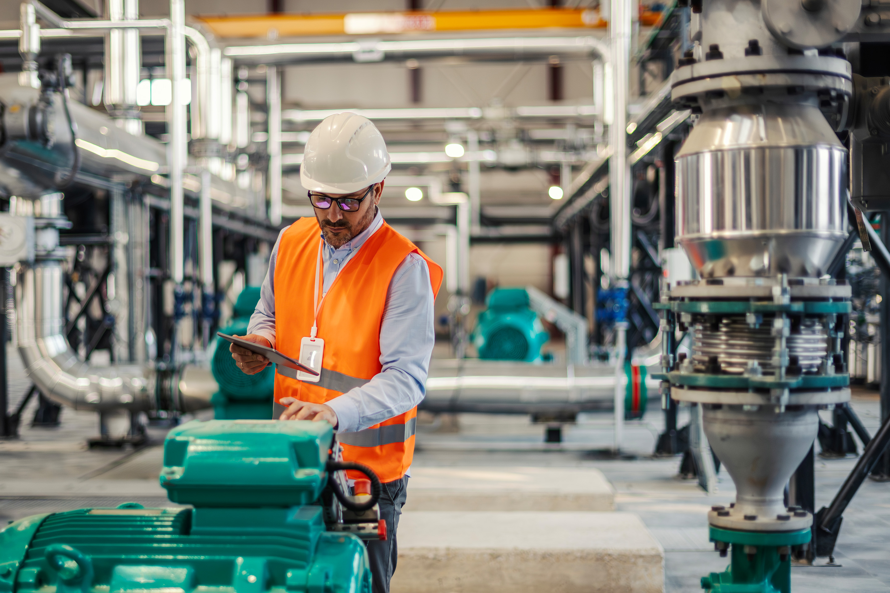 Engineer inspecting industrial pumping equipment using a tablet, representing fluid handling systems, plant reliability, and process optimisation in industrial operations.