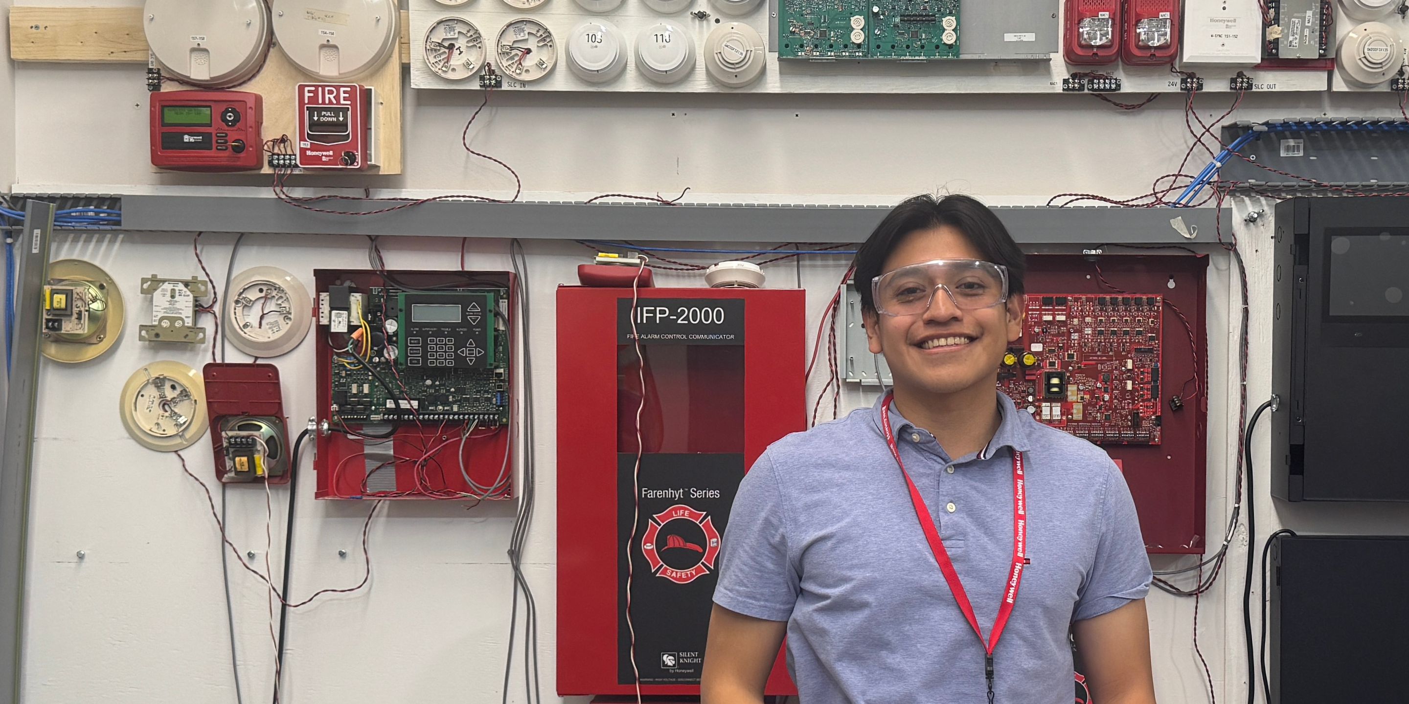 Certification engineer Edwin Rosales smiles in front of a wall with Honeywell fire safety technologies.