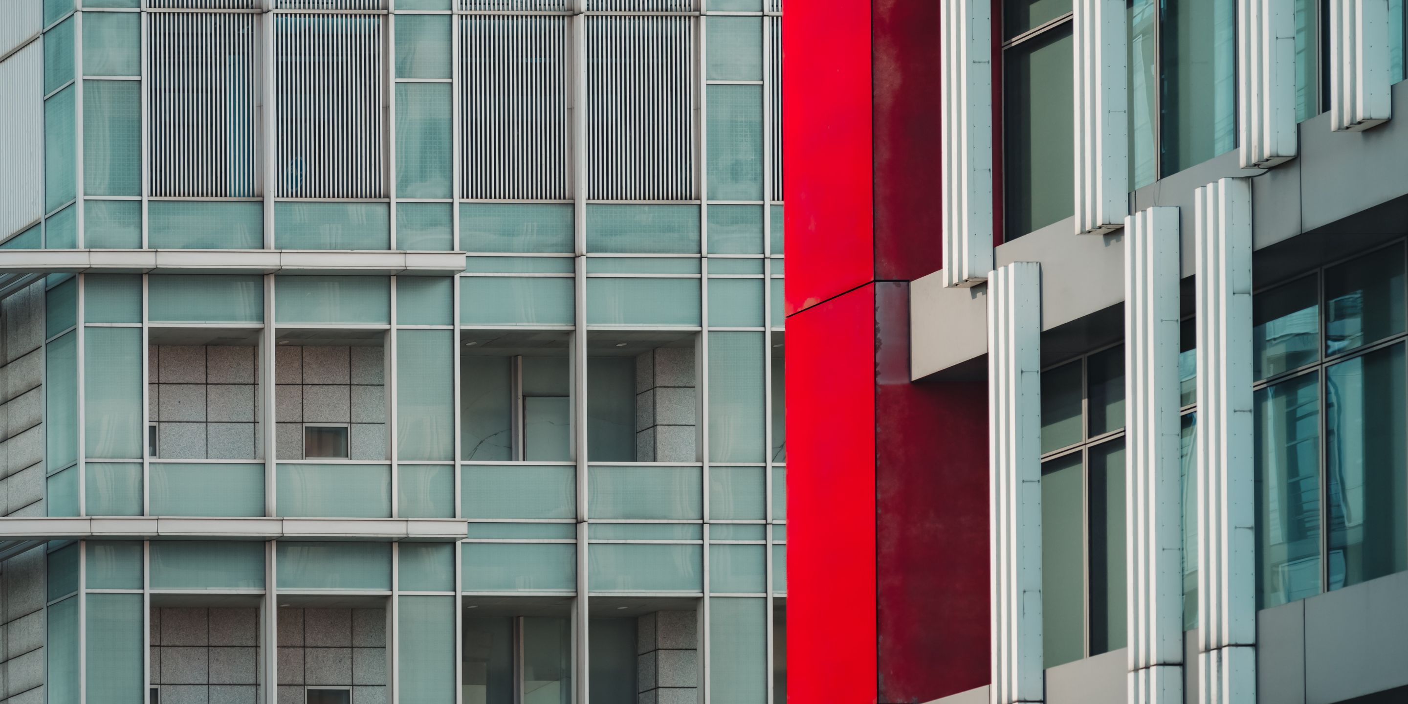 Close-up view of two modern city buildings/windows in grey, with a red accent pillar.