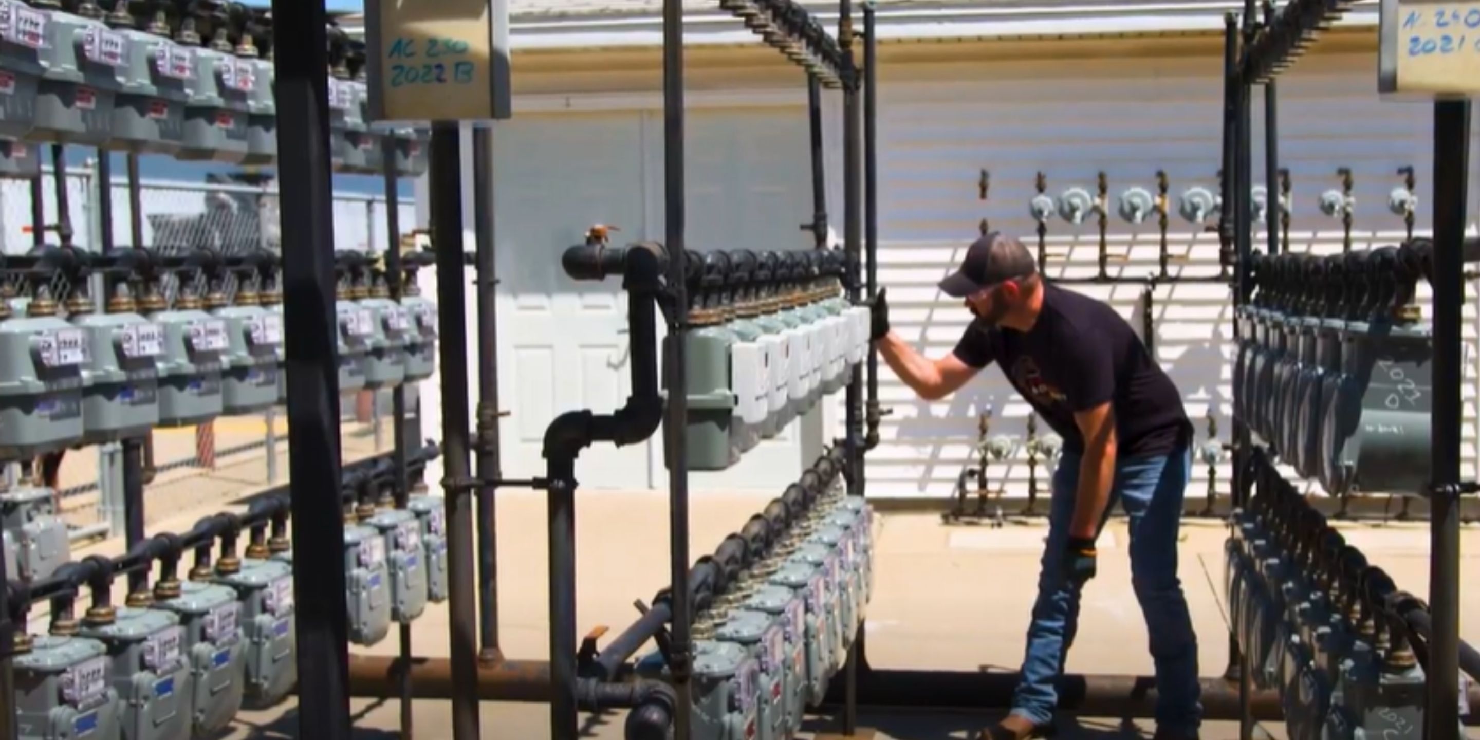 A skilled technician is seen inspecting and maintaining a series of industrial gas meters arranged in rows at an outdoor facility. The image highlights the importance of regular maintenance and monitoring for efficient gas distribution.