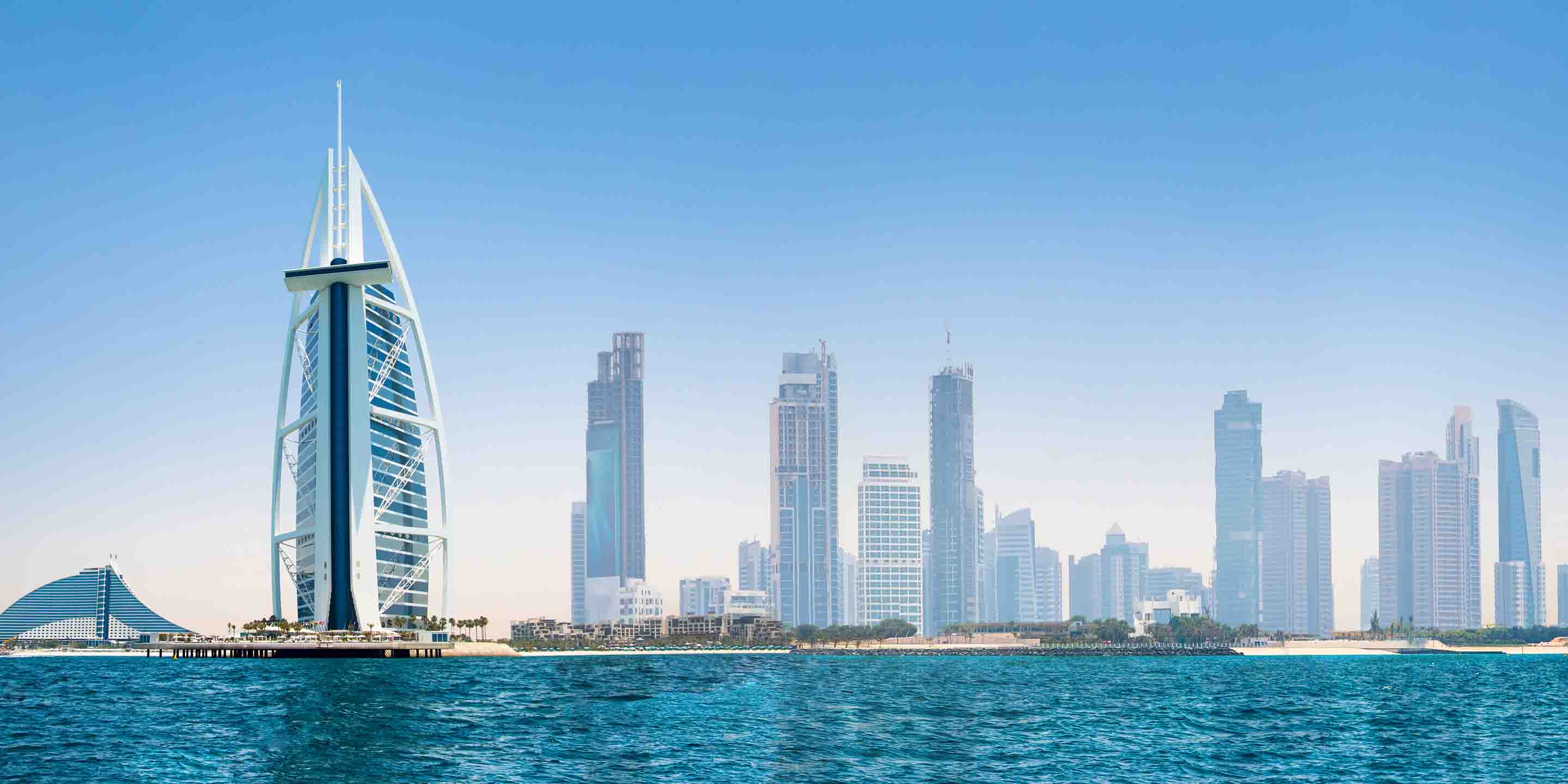 Stunning view of Dubai's skyline featuring the iconic Burj Al Arab and modern skyscrapers against a clear blue sky and the Arabian Gulf.
