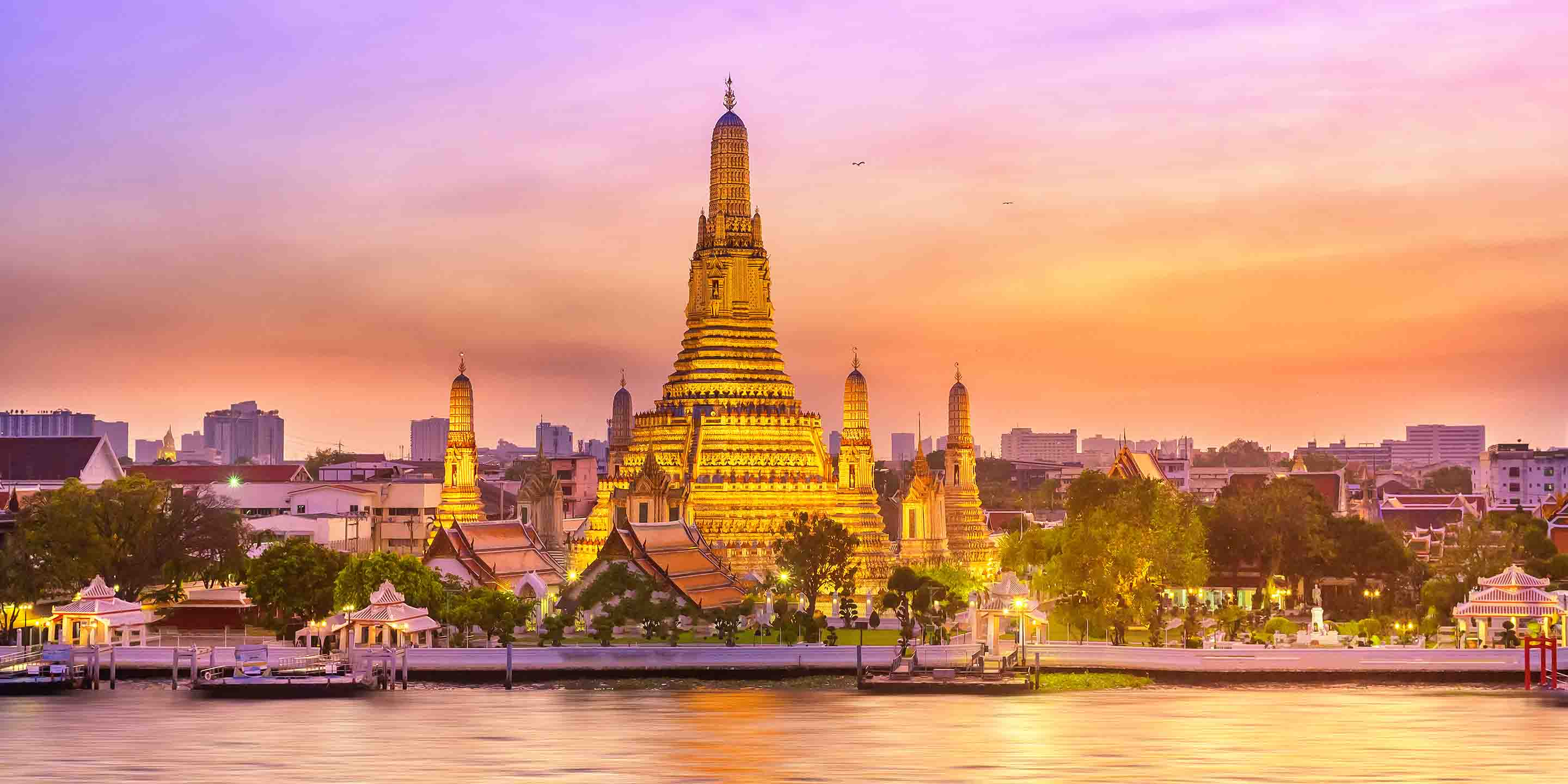 Captivating view of Wat Arun at sunset, highlighting its intricate architecture against a pastel sky, with the Chao Phraya River in the foreground.