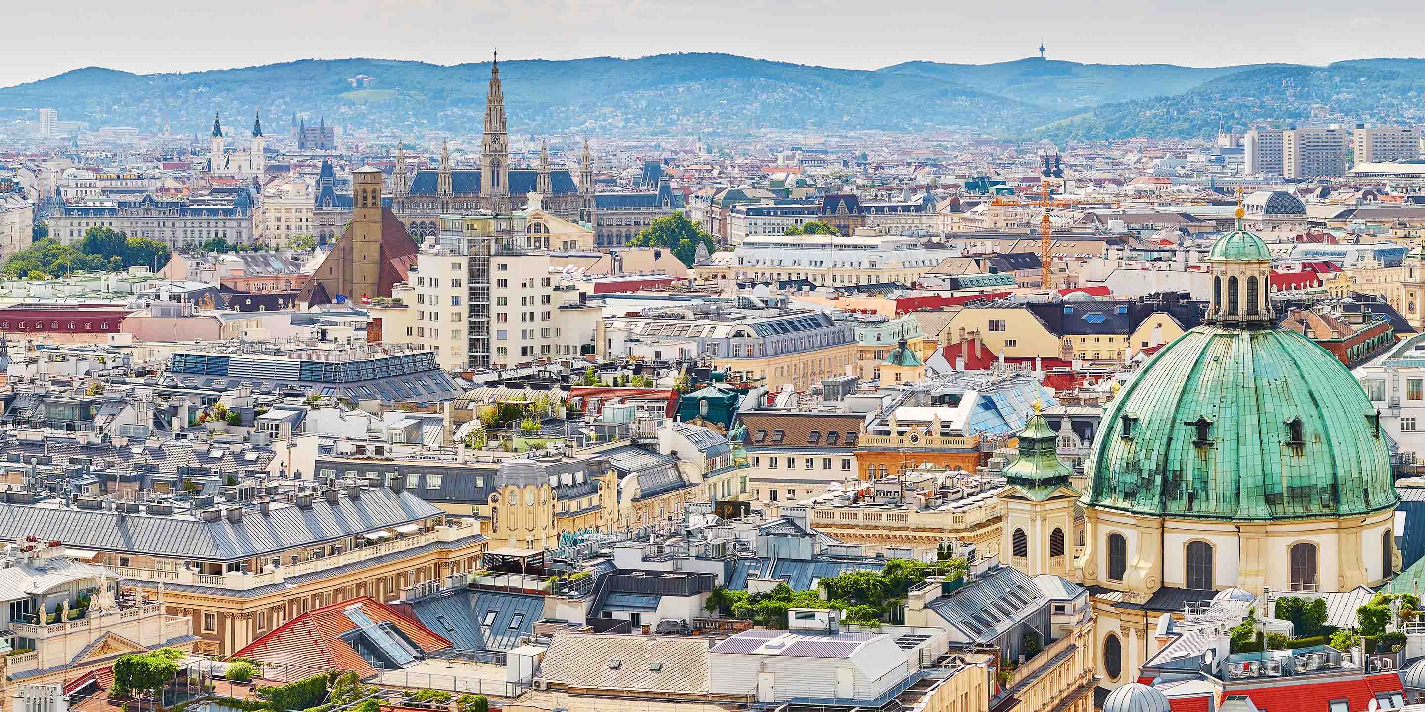 A stunning aerial view of Vienna, showcasing historic architecture, rooftops, and distant hills under a cloudy sky.